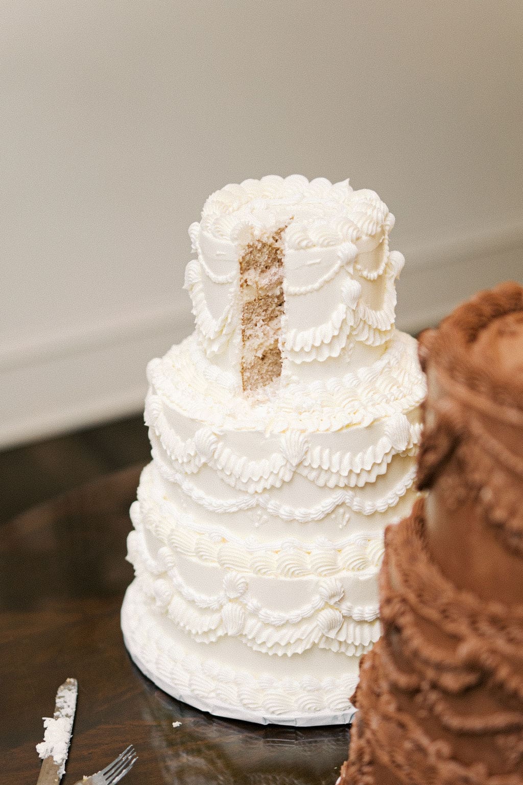 Classic white tiered wedding cake with intricate piping and a slice cut out during a timeless Mansion Wedding reception.