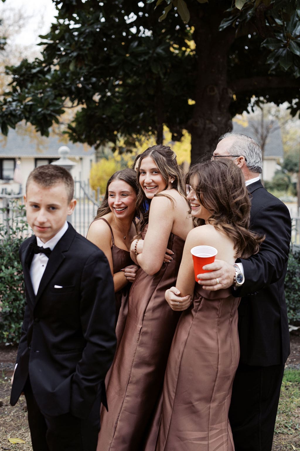 Group of wedding guests smiling and embracing outdoors during the celebration.