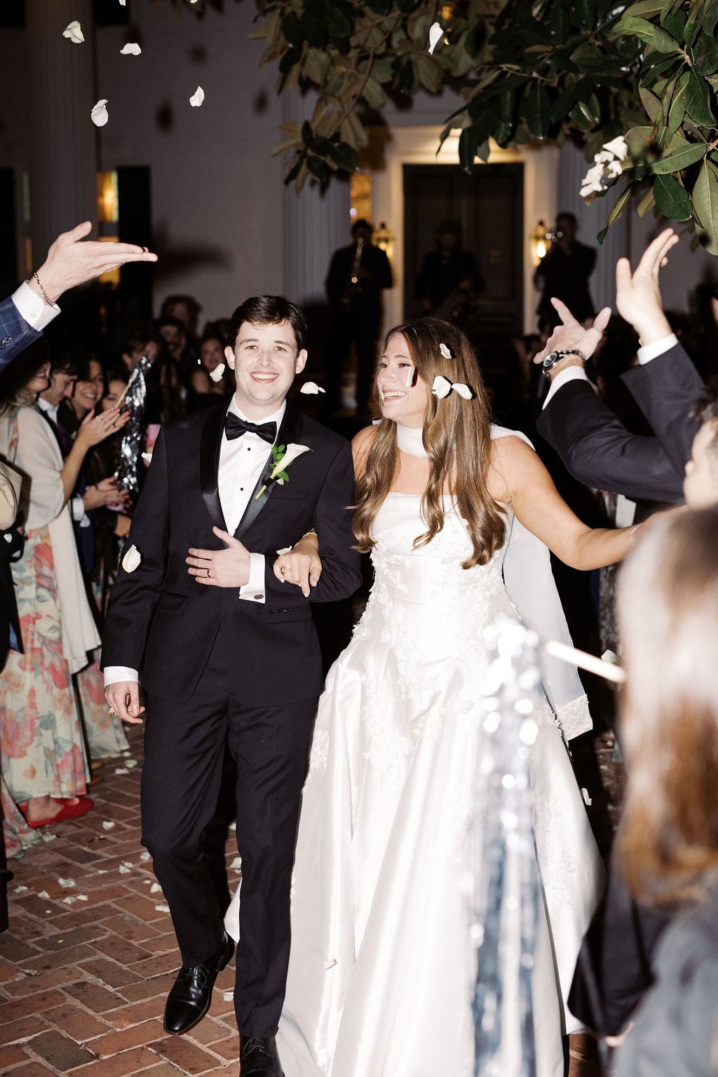 Newlyweds walking hand in hand through cheering guests while flower petals fall during their wedding exit.