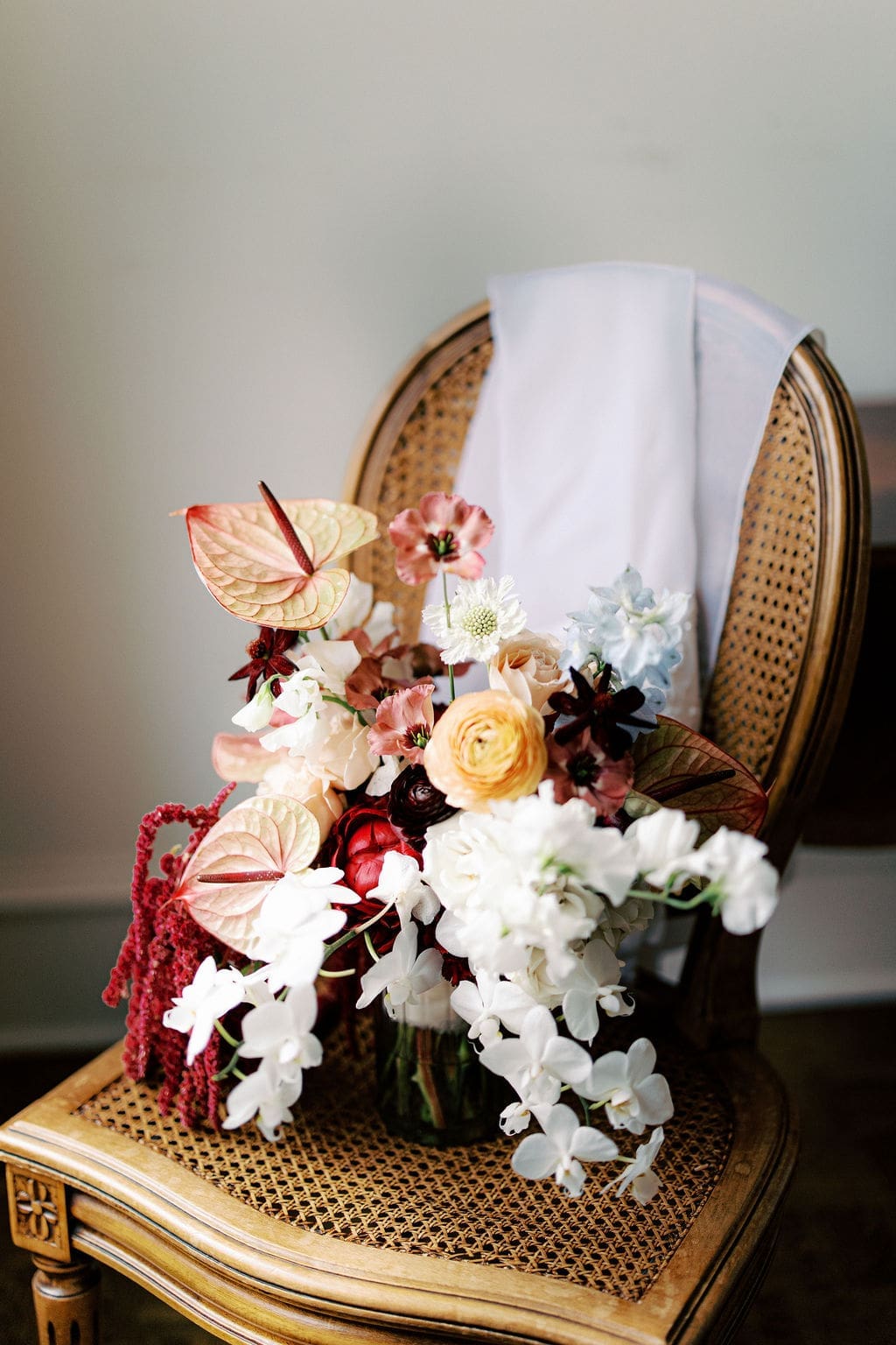 Elegant bridal bouquet with orchids, anthurium, and rich autumn tones photographed on a vintage chair during a romantic Mansion Wedding morning.