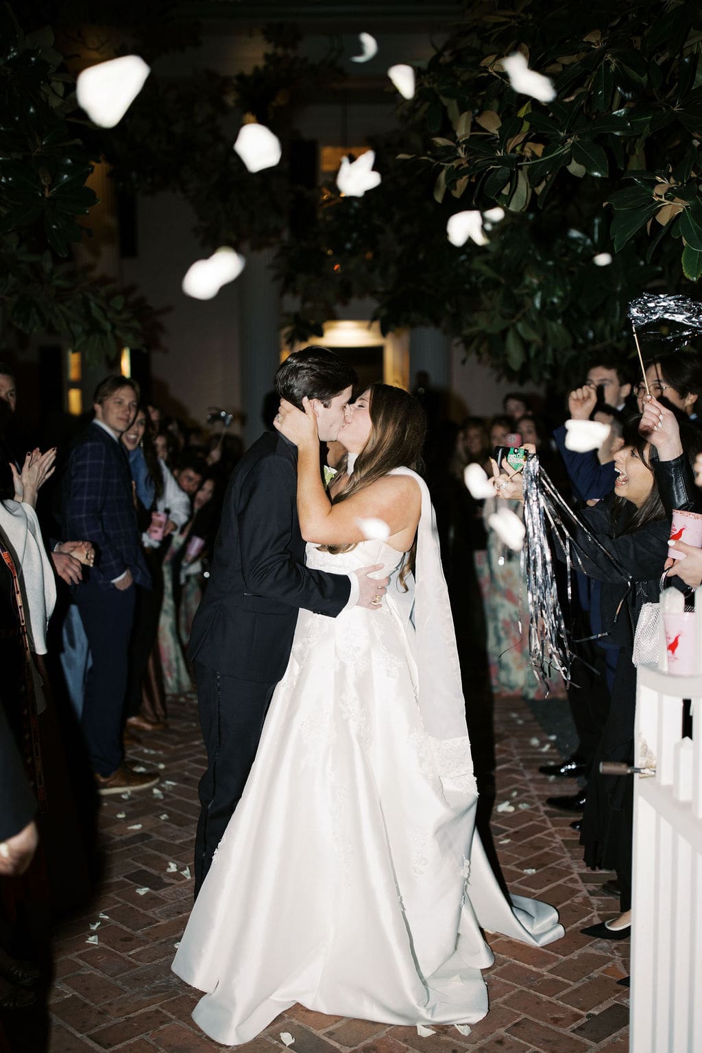 Bride and groom sharing a kiss during their joyful send-off as guests toss petals at a romantic Mansion Wedding celebration.