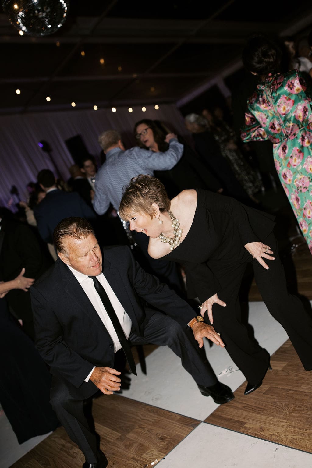 Wedding guests dancing energetically on a brown-and-white dance floor during the reception.