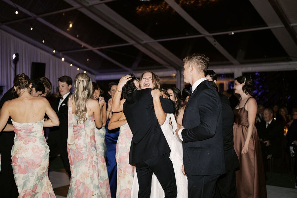 Bride hugging a guest on the dance floor while friends celebrate during a lively Mansion Wedding reception.