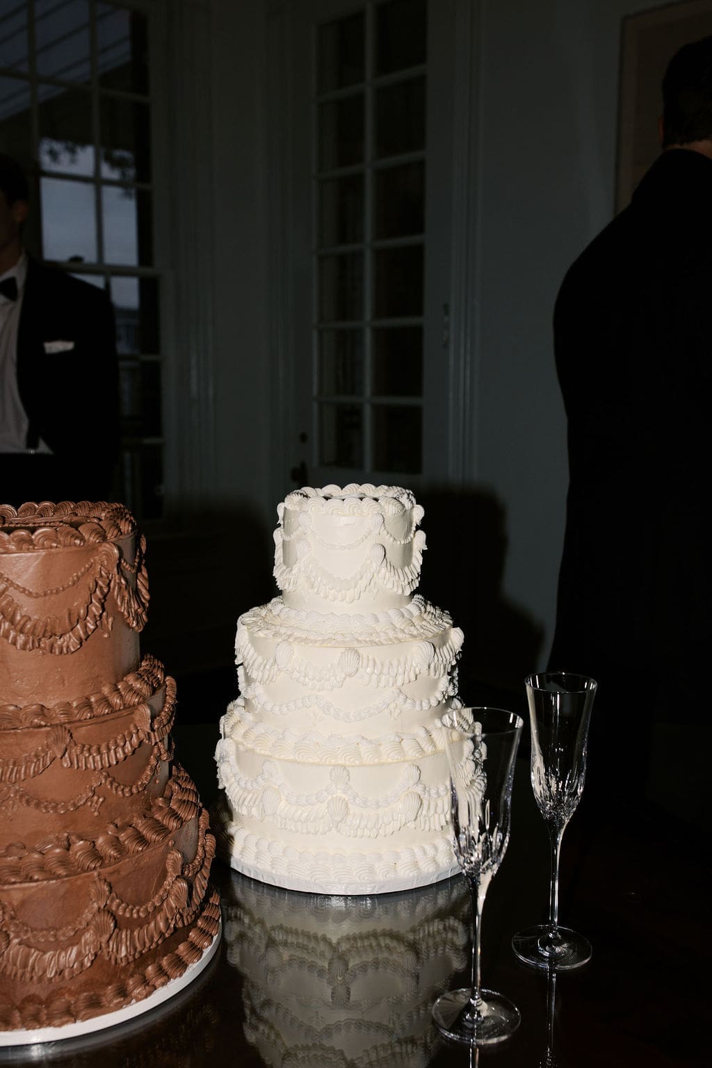 Elegant chocolate and vanilla tiered wedding cakes displayed with champagne flutes during the reception.