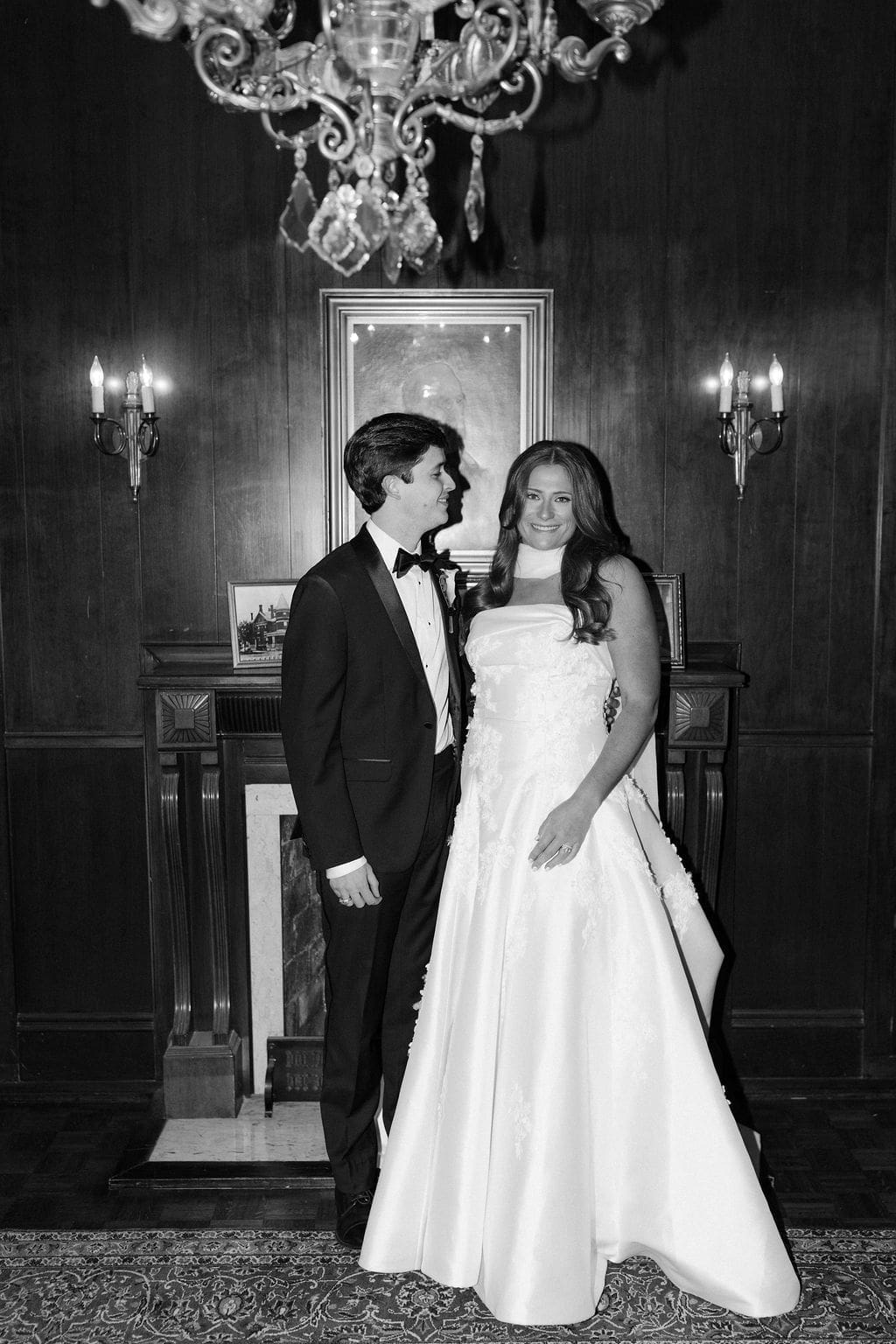 Bride and groom standing together inside a dark wood-paneled room with vintage portraits during a timeless Mansion Wedding portrait.