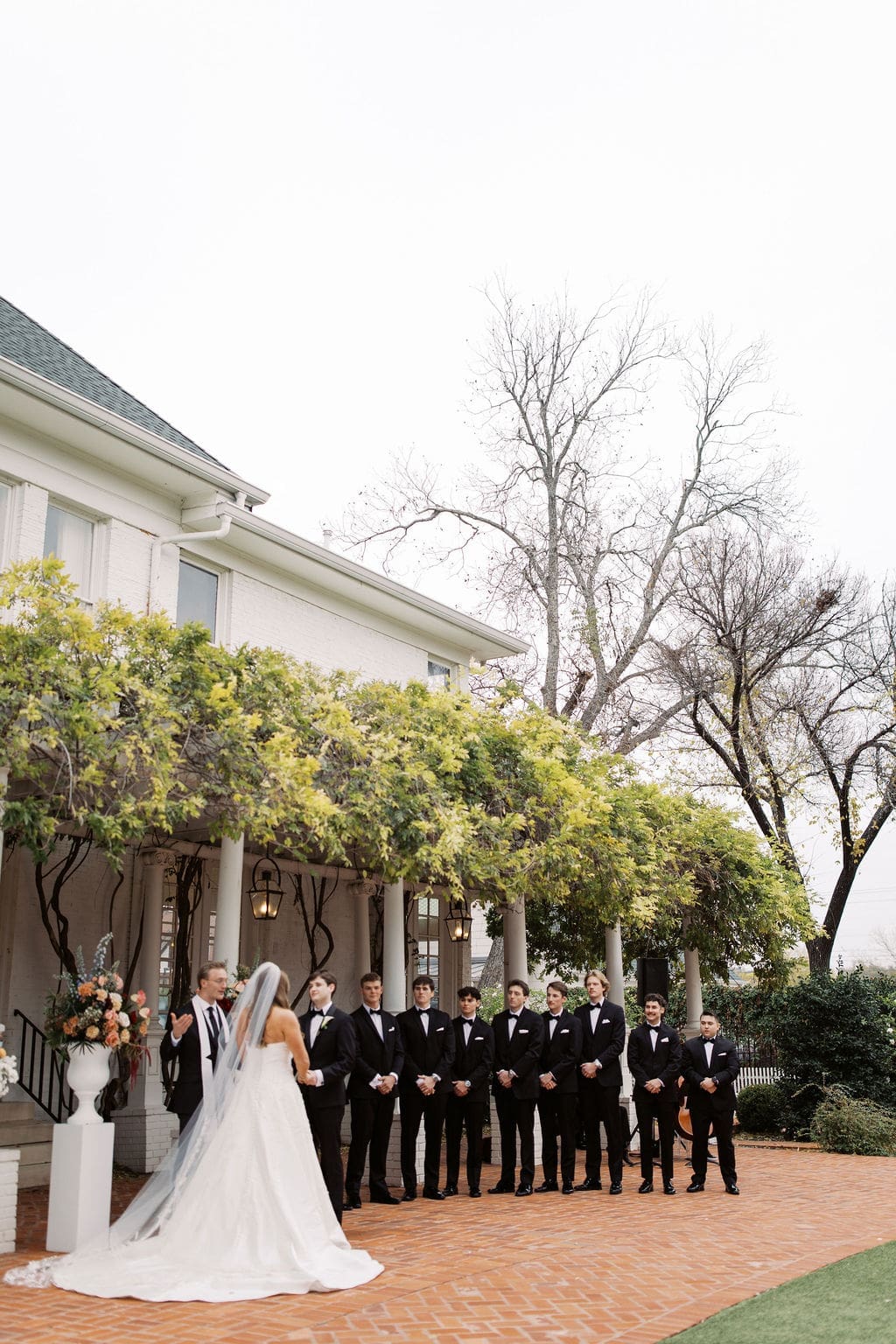 Bride and groom exchanging vows in front of the estate porch surrounded by groomsmen during a romantic Mansion Wedding ceremony.