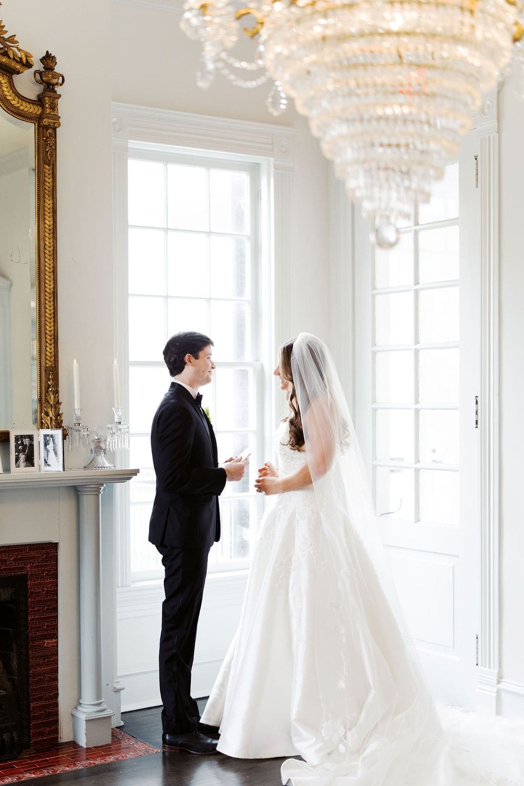 Bride and groom sharing a quiet moment indoors near a fireplace and chandelier during their wedding day portraits.