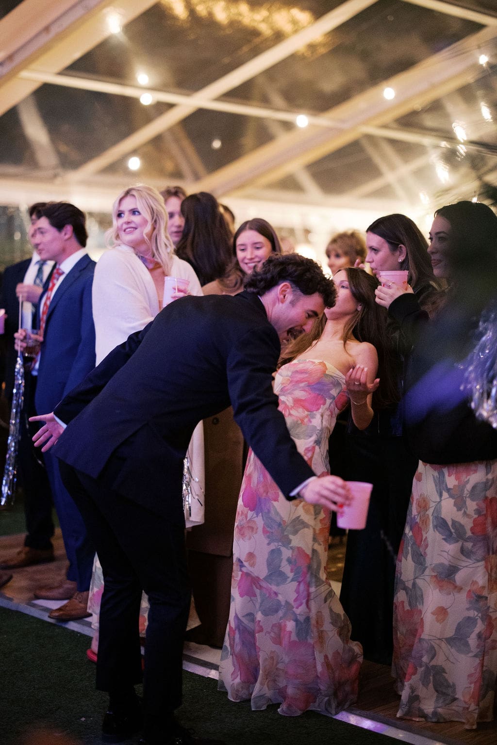 Wedding guests dancing together with drinks in hand during a fun reception party.