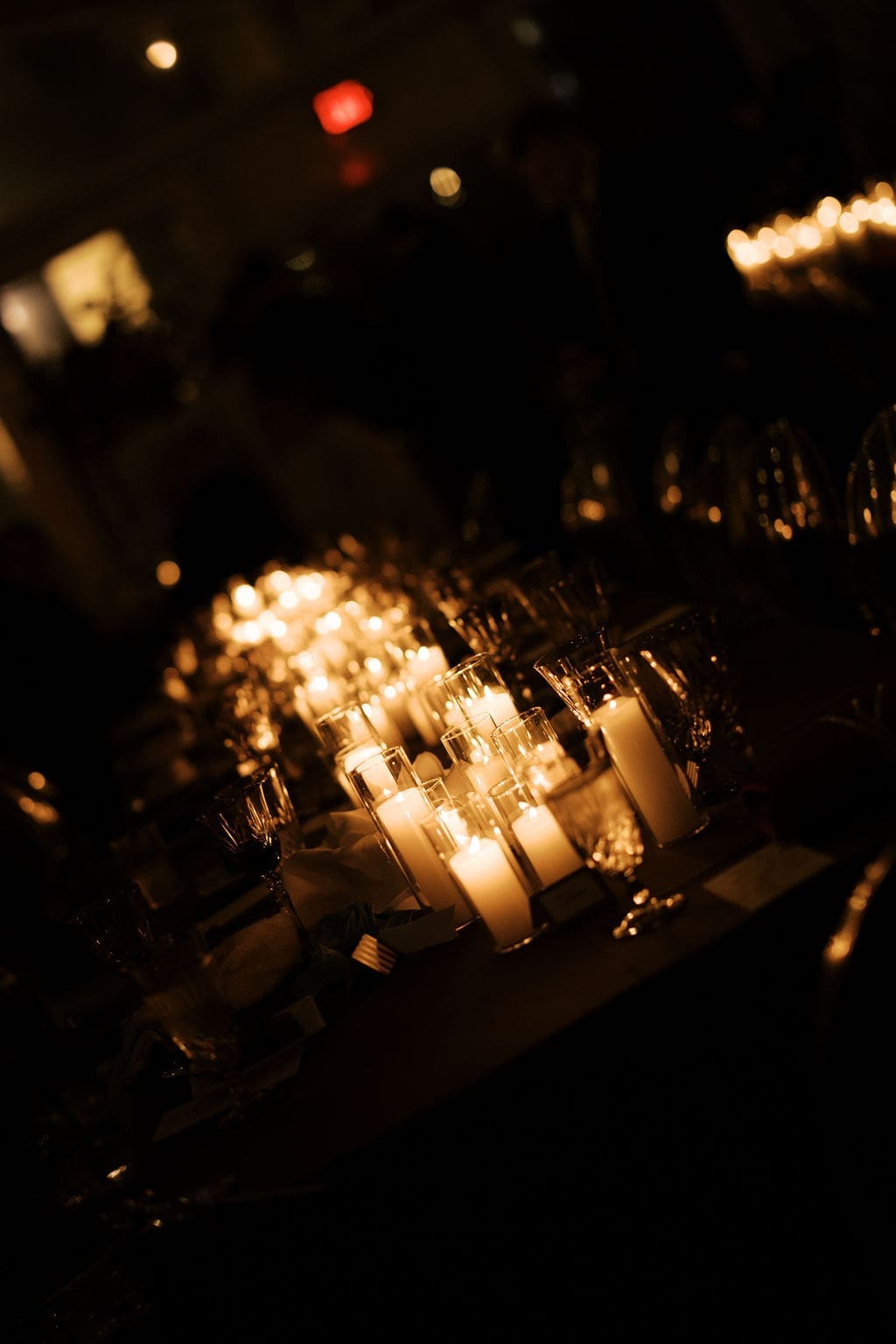 Dramatic candlelit reception table with glowing glass votives creating a warm evening atmosphere.