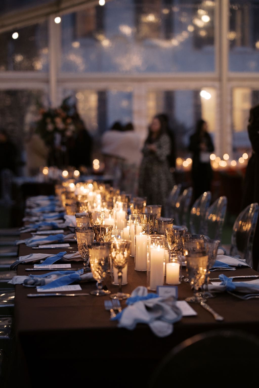 Elegant reception table filled with glowing candles, glassware, and place settings inside a romantic evening reception space.