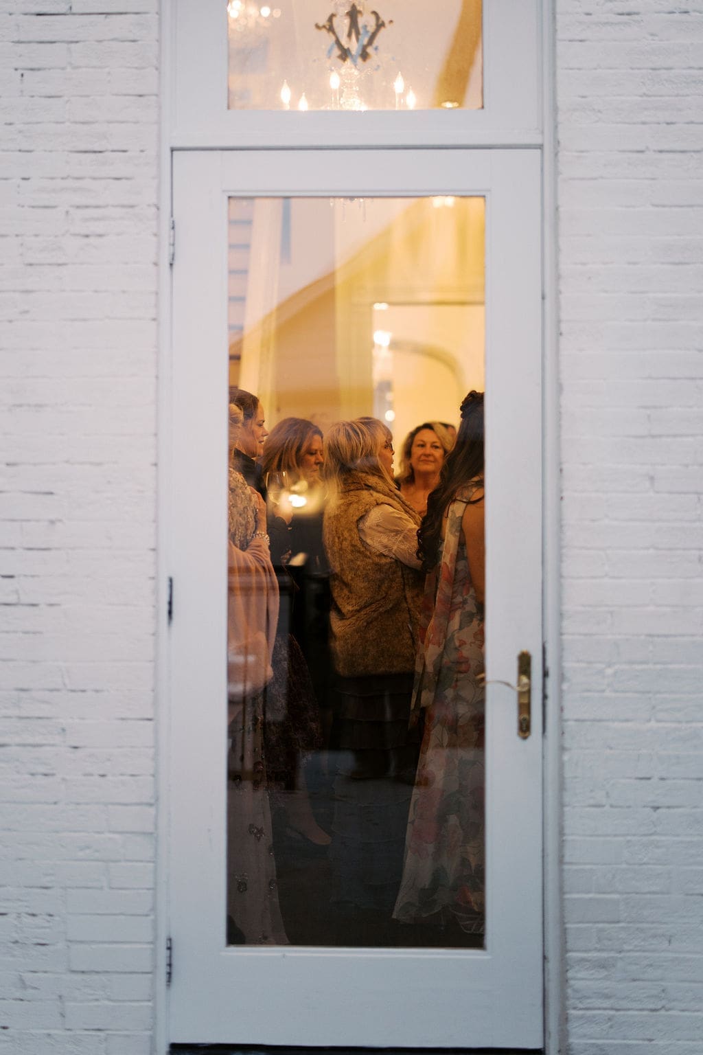 Guests gathered inside a glowing reception space seen through a glass door during an elegant Mansion Wedding celebration.