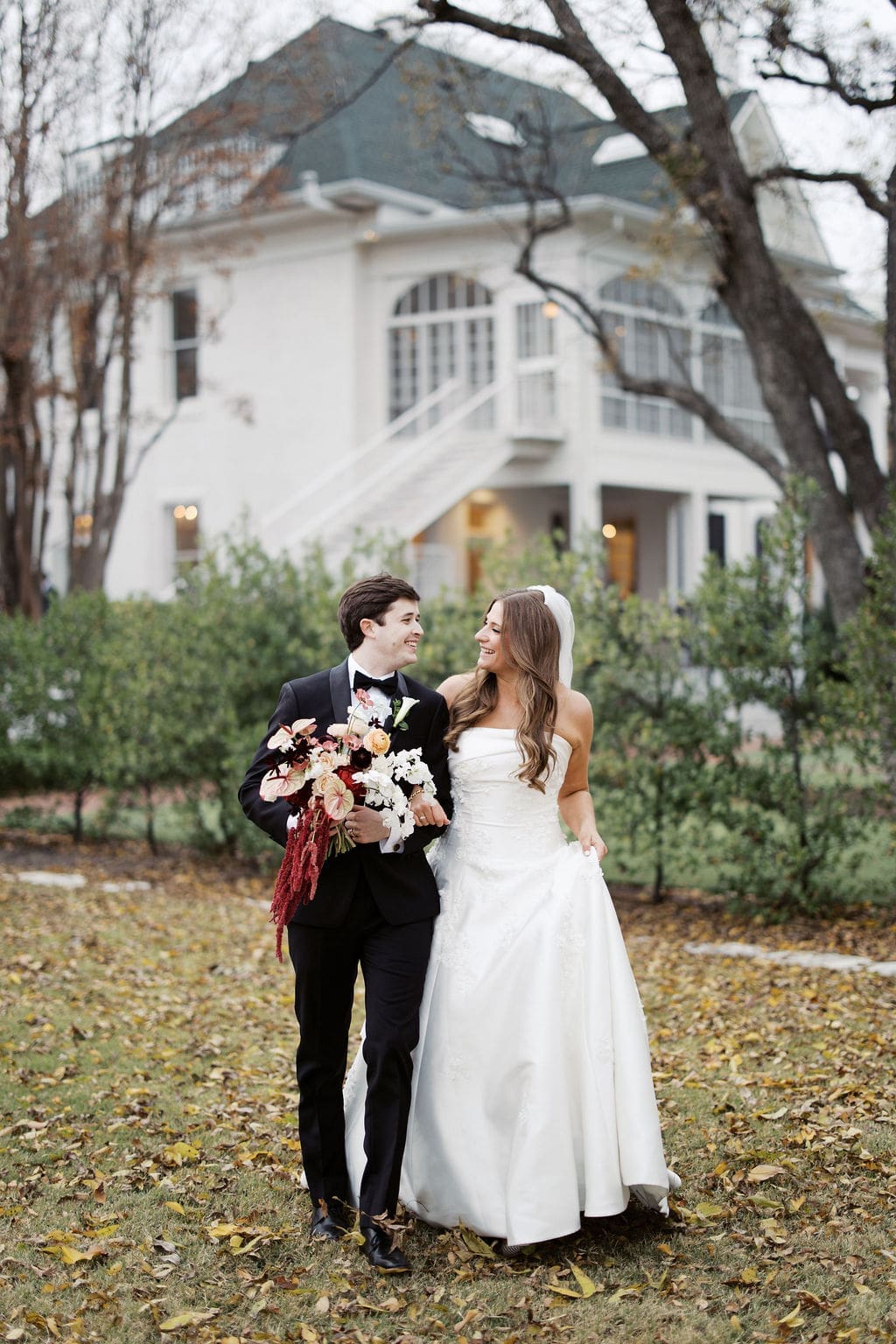 Newlyweds strolling together across the lawn in front of a beautiful white estate during a romantic Mansion Wedding portrait.