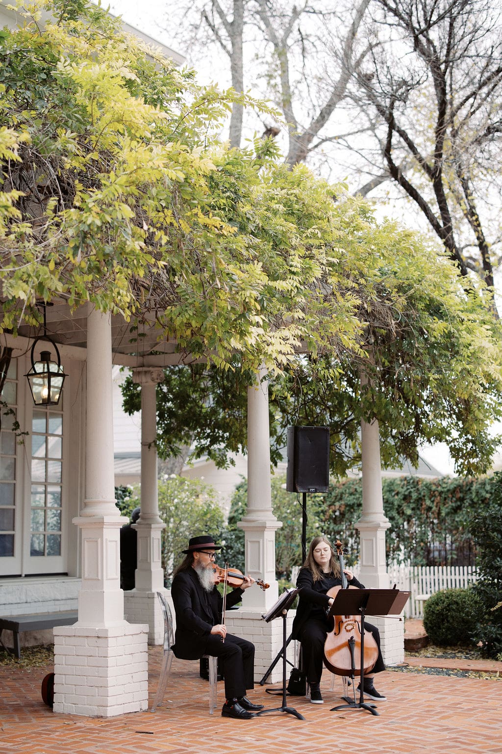 String musicians performing beneath a vine-covered porch during a romantic outdoor Mansion Wedding ceremony.