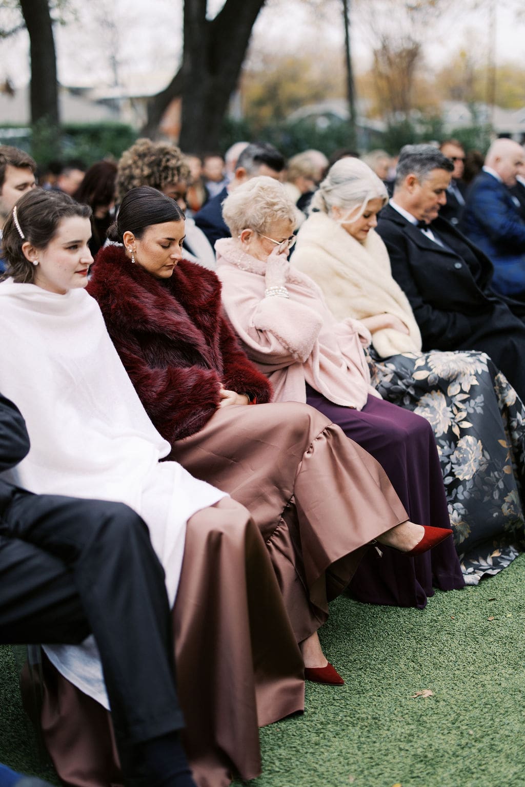 Wedding guests seated outdoors in coats and formal attire during the ceremony on a cool autumn day.