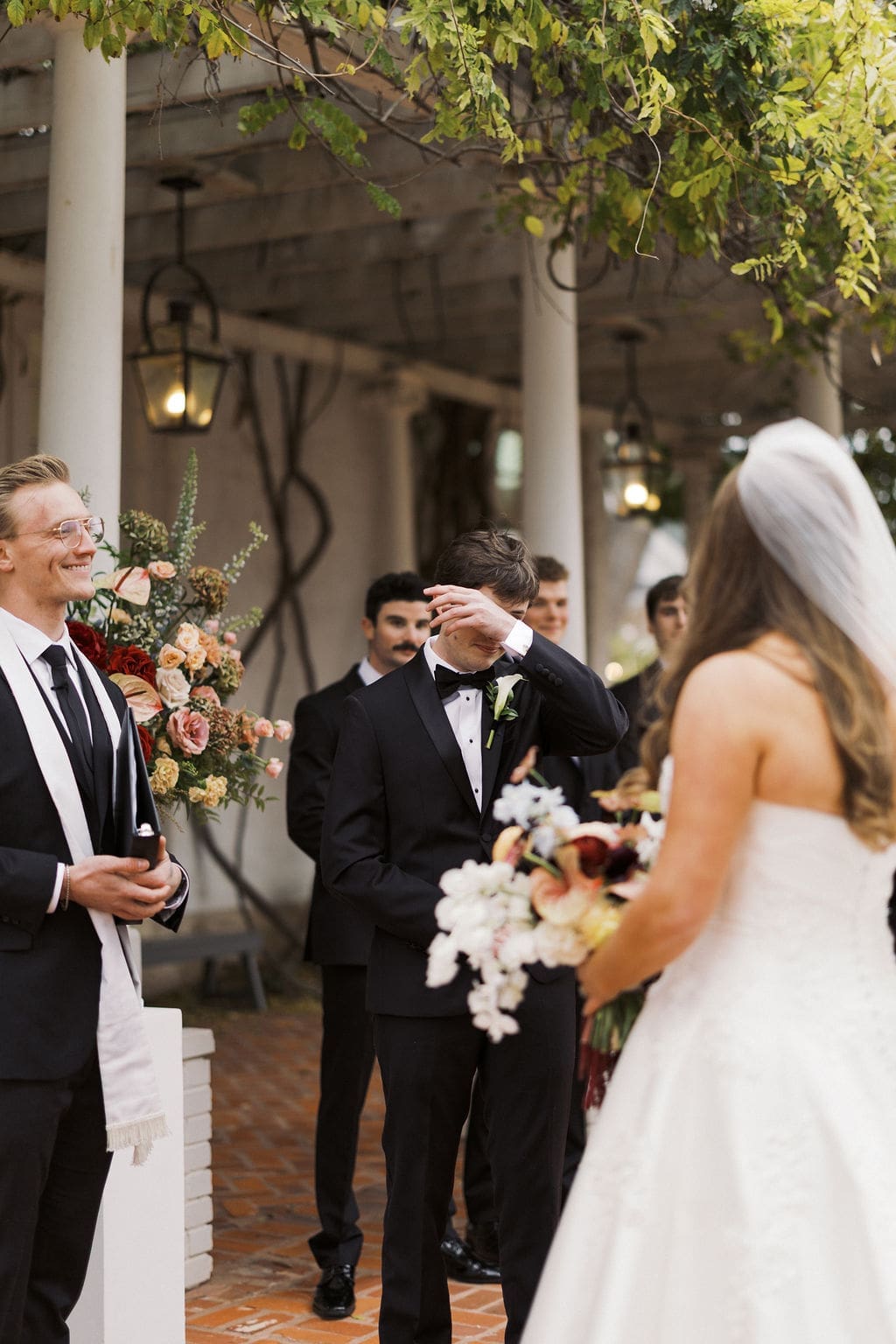 Groom wiping away tears during an emotional ceremony moment as the bride approaches the altar.