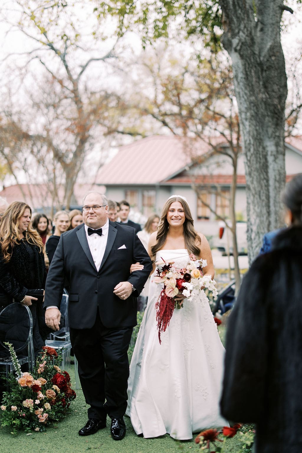 Bride walking down the aisle with her father during an emotional outdoor Mansion Wedding ceremony surrounded by fall florals.