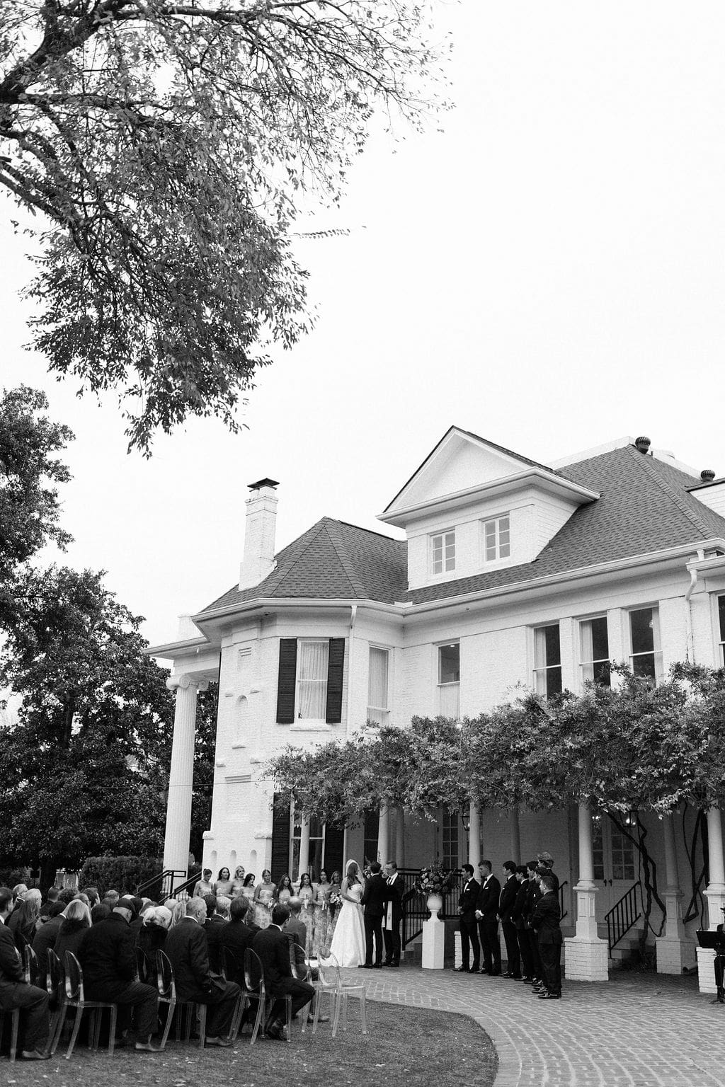 Wide view of guests gathered for an outdoor ceremony in front of a historic white estate during a romantic Mansion Wedding.