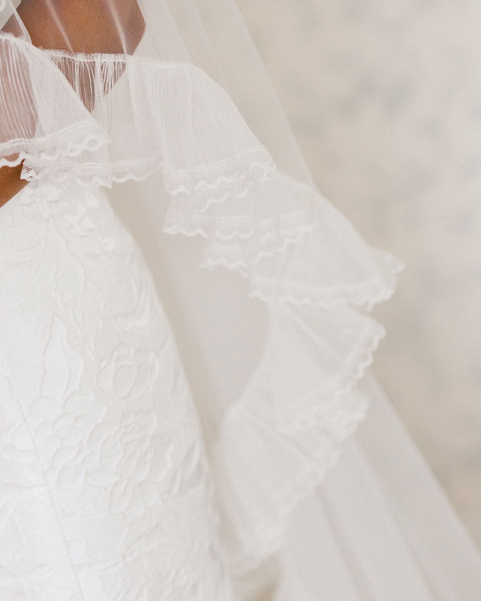 Detail shot of bridal portraits featuring the intricate lace texture of a wedding gown alongside the delicate ruffled edge of a layered tulle veil