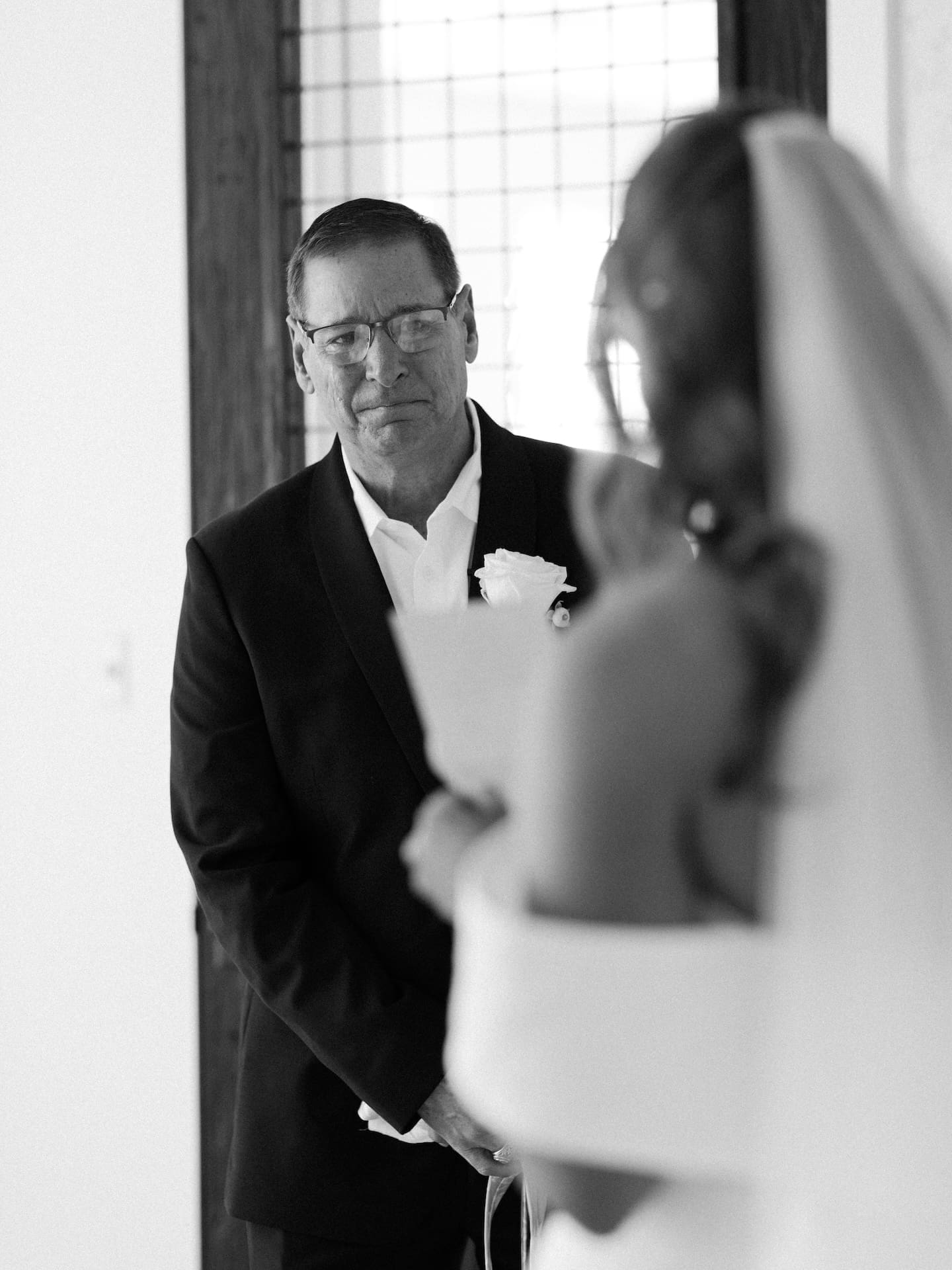 A black and white film photo of the father of the bride looking at his daughter with pure emotion during their first look at Camp Hosea.