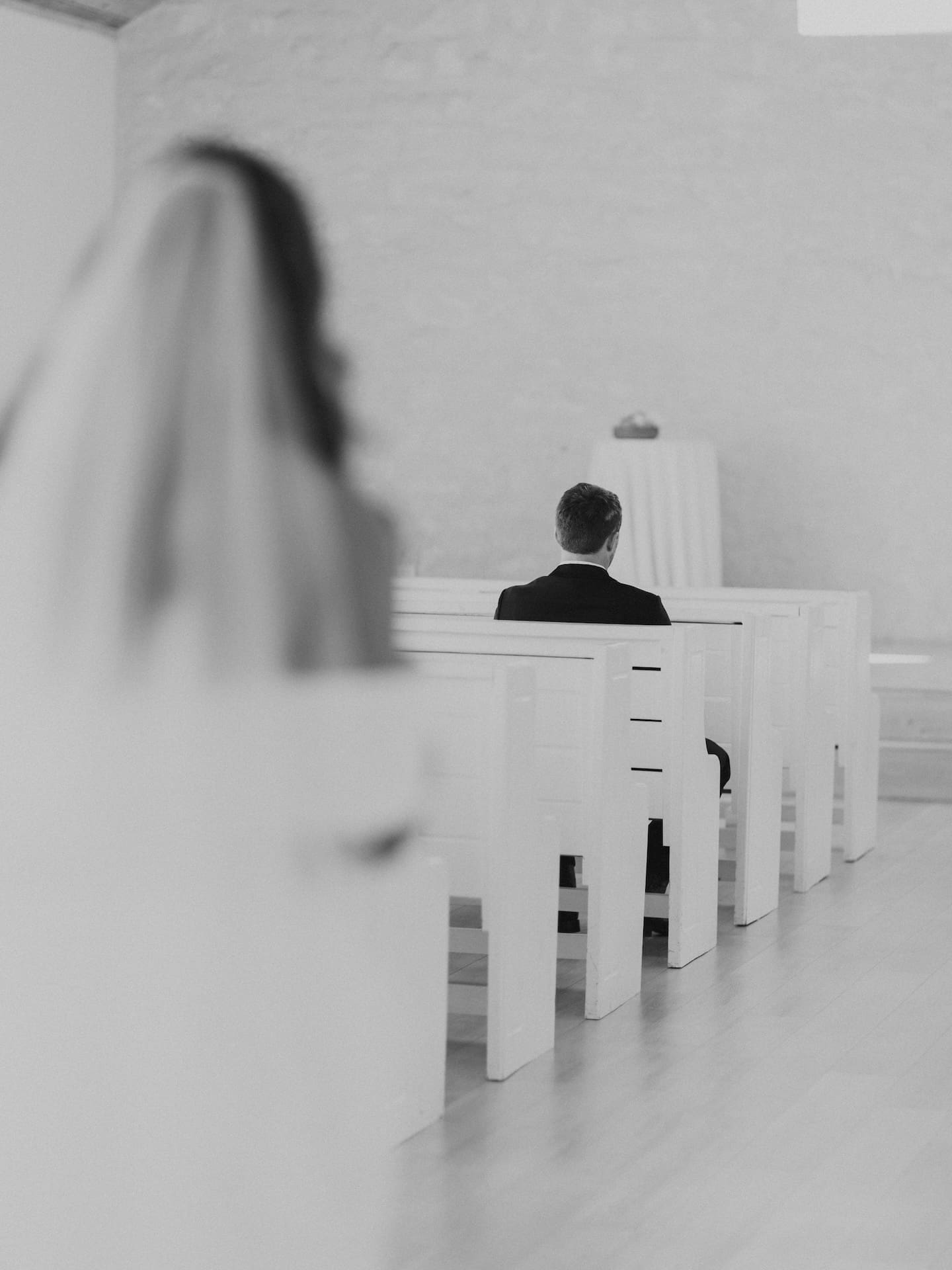 The groom waits in the chapel pew at Camp Hosea as the bride approaches for their private first look, her veil blurred softly in the foreground.