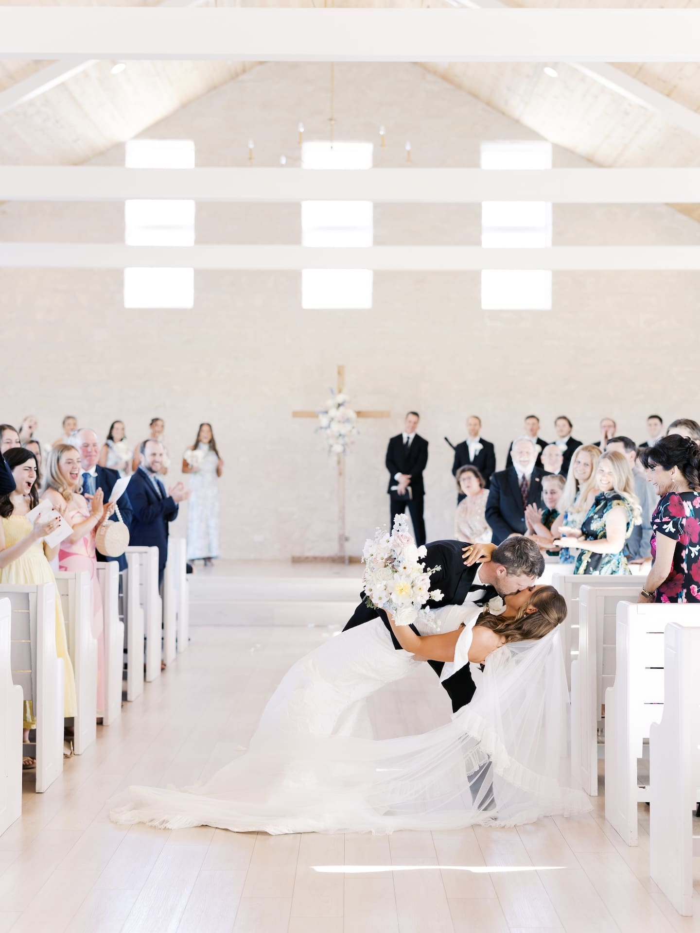 The groom dips the bride for a kiss at the end of the aisle inside the Camp Hosea chapel, the whole room erupting in cheers around them.