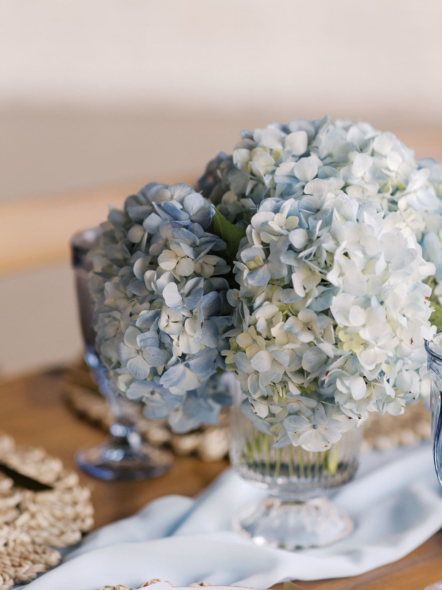 Pale blue and white hydrangeas spill from glass vases on the reception tables, styled with a dusty blue linen runner.