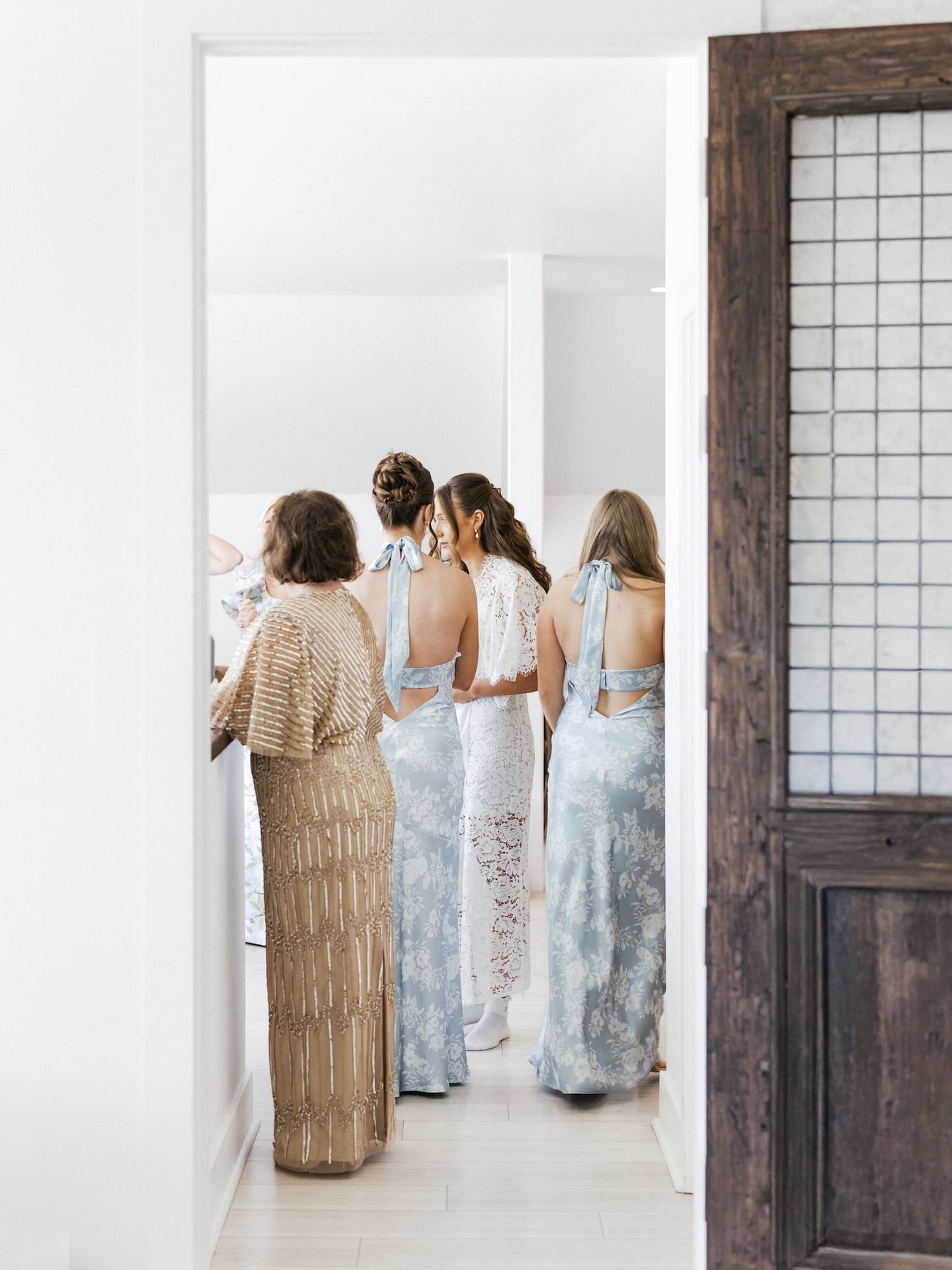 Framed through a doorway at Camp Hosea, the bride is surrounded by her bridesmaids and mother in a tender getting-ready moment before the ceremony.
