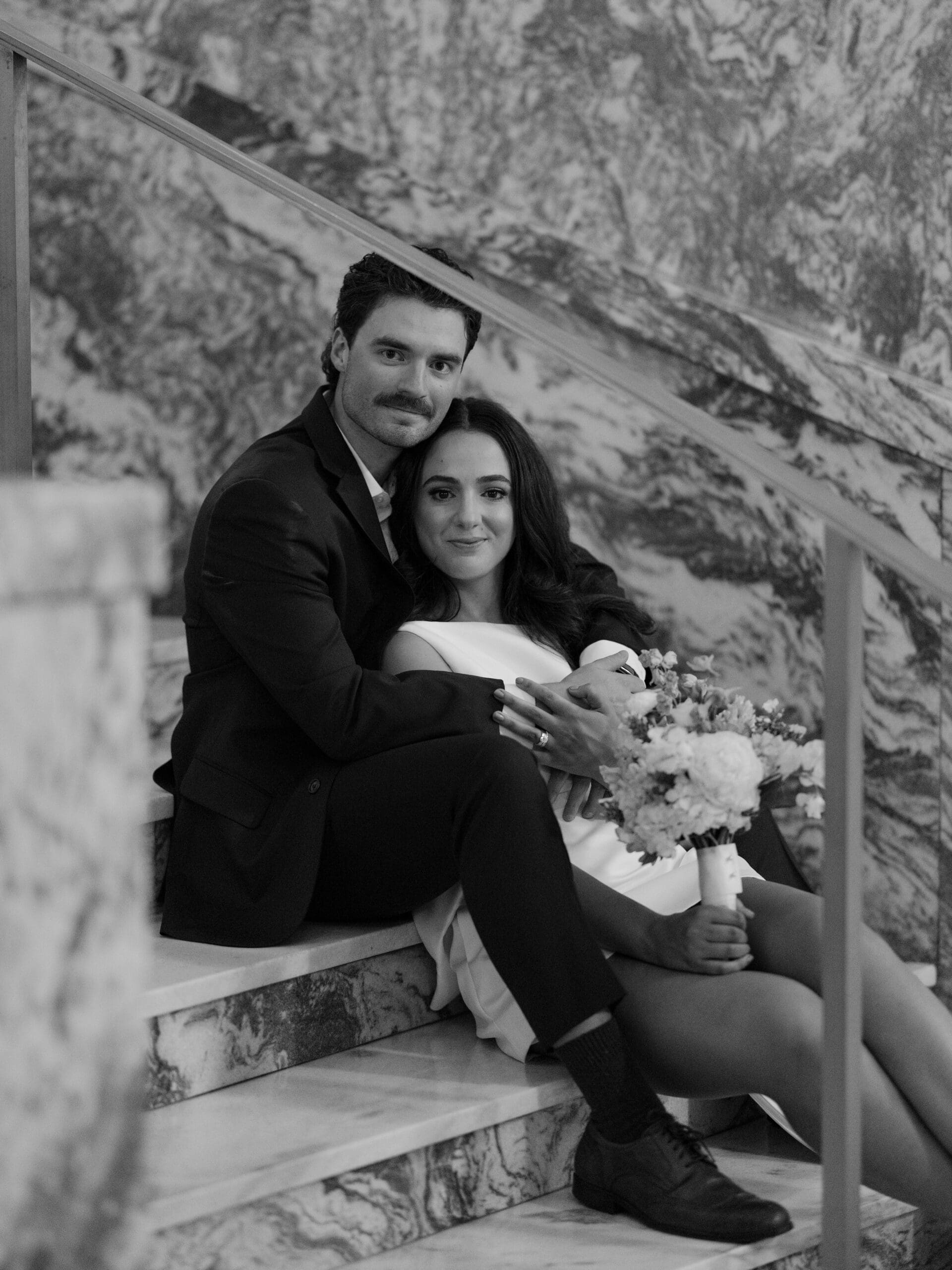 Bride and groom sitting together on a marble staircase in black and white
