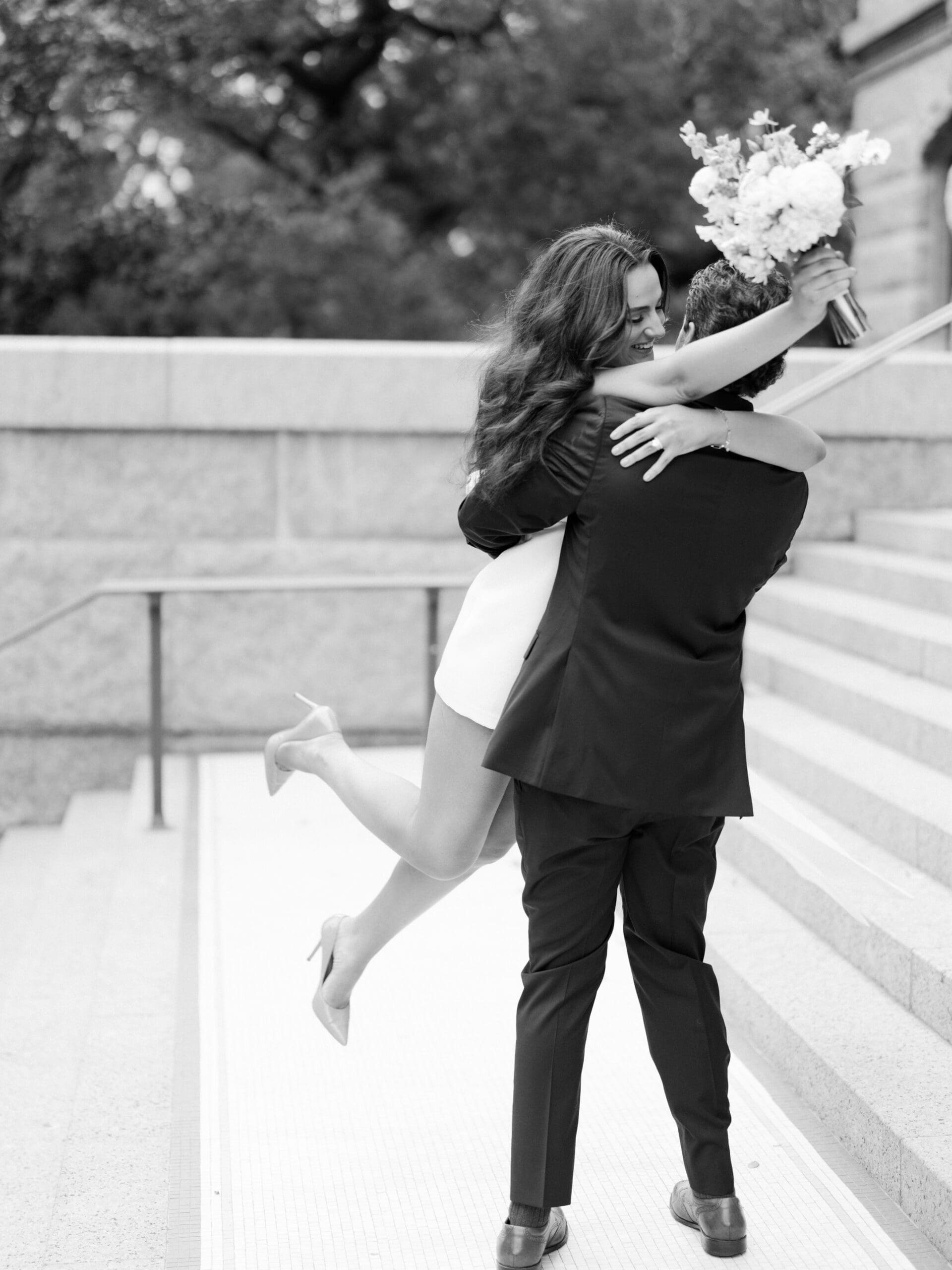 Groom lifting bride on courthouse steps in a joyful black and white photo
