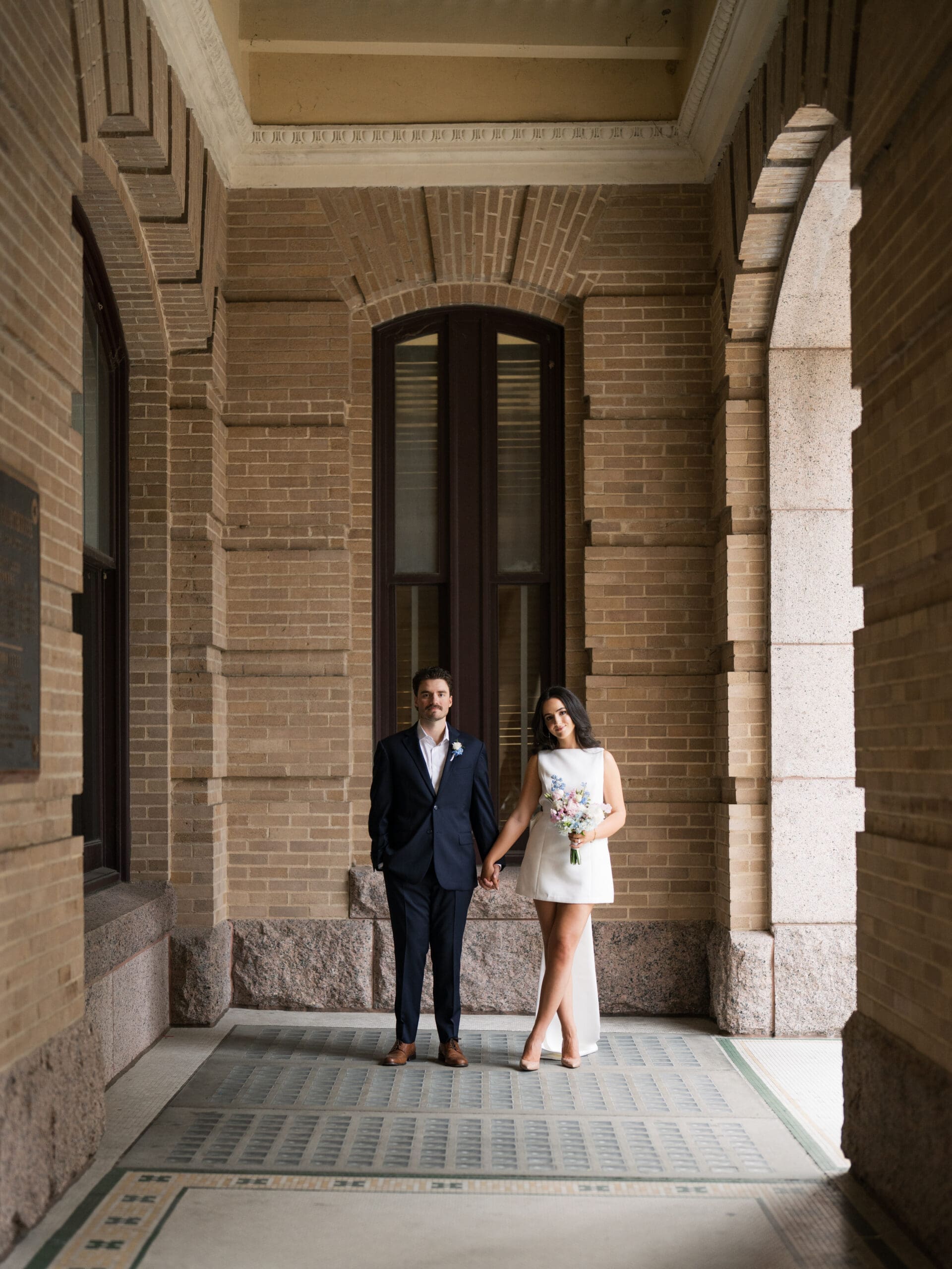 Bride and groom standing hand in hand in a warm brick archway at their courthouse wedding in Houston
