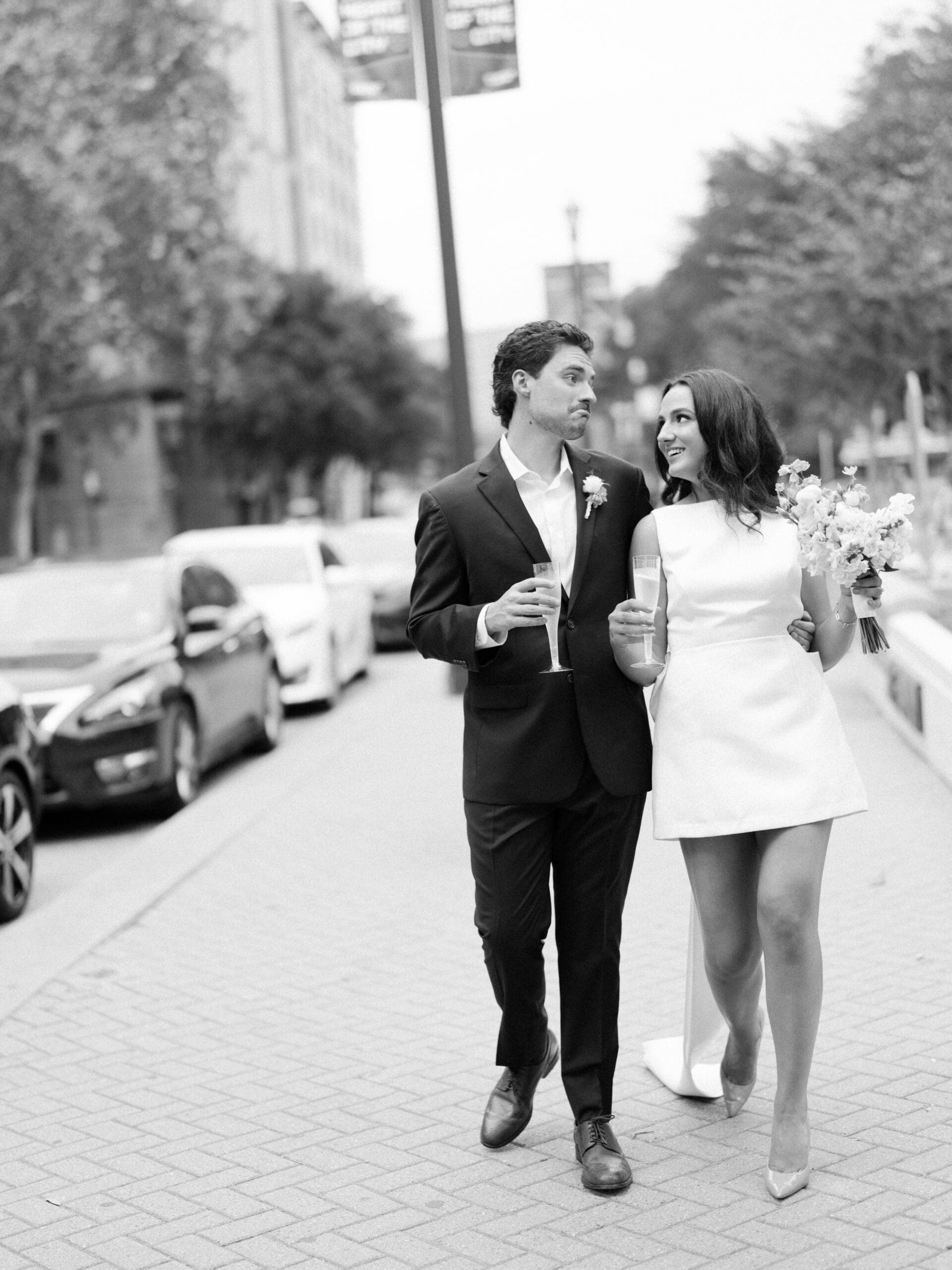 Couple strolling down a downtown sidewalk with champagne glasses in black and white
