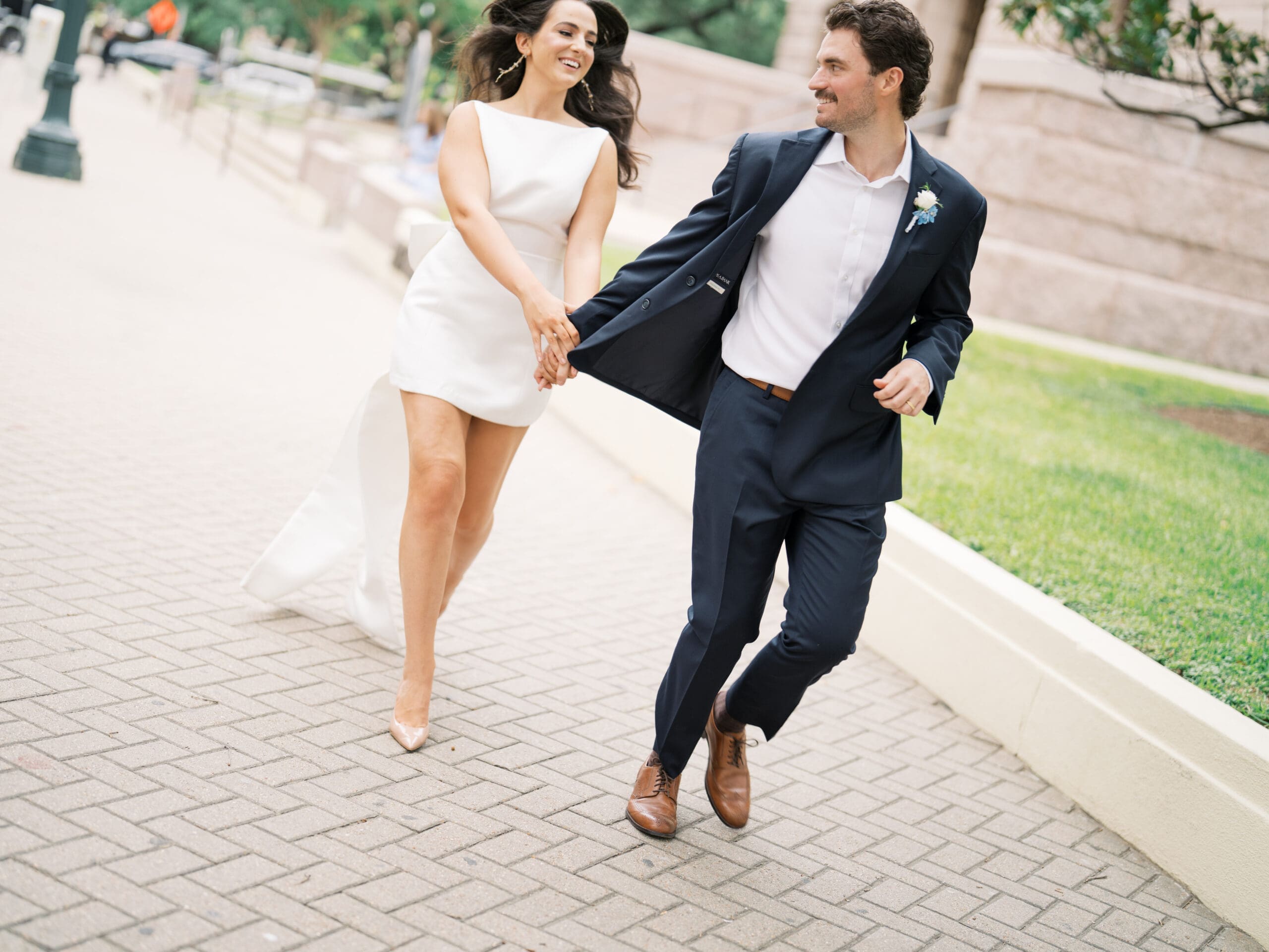 Bride and groom laughing and running hand in hand along a brick path during their courthouse wedding in Houston
