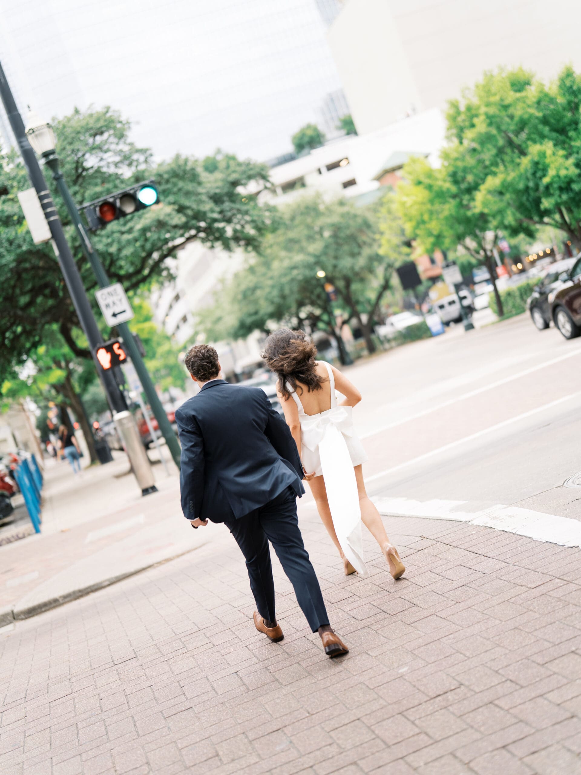 Bride and groom seen from behind as they dash across a downtown Houston street corner
