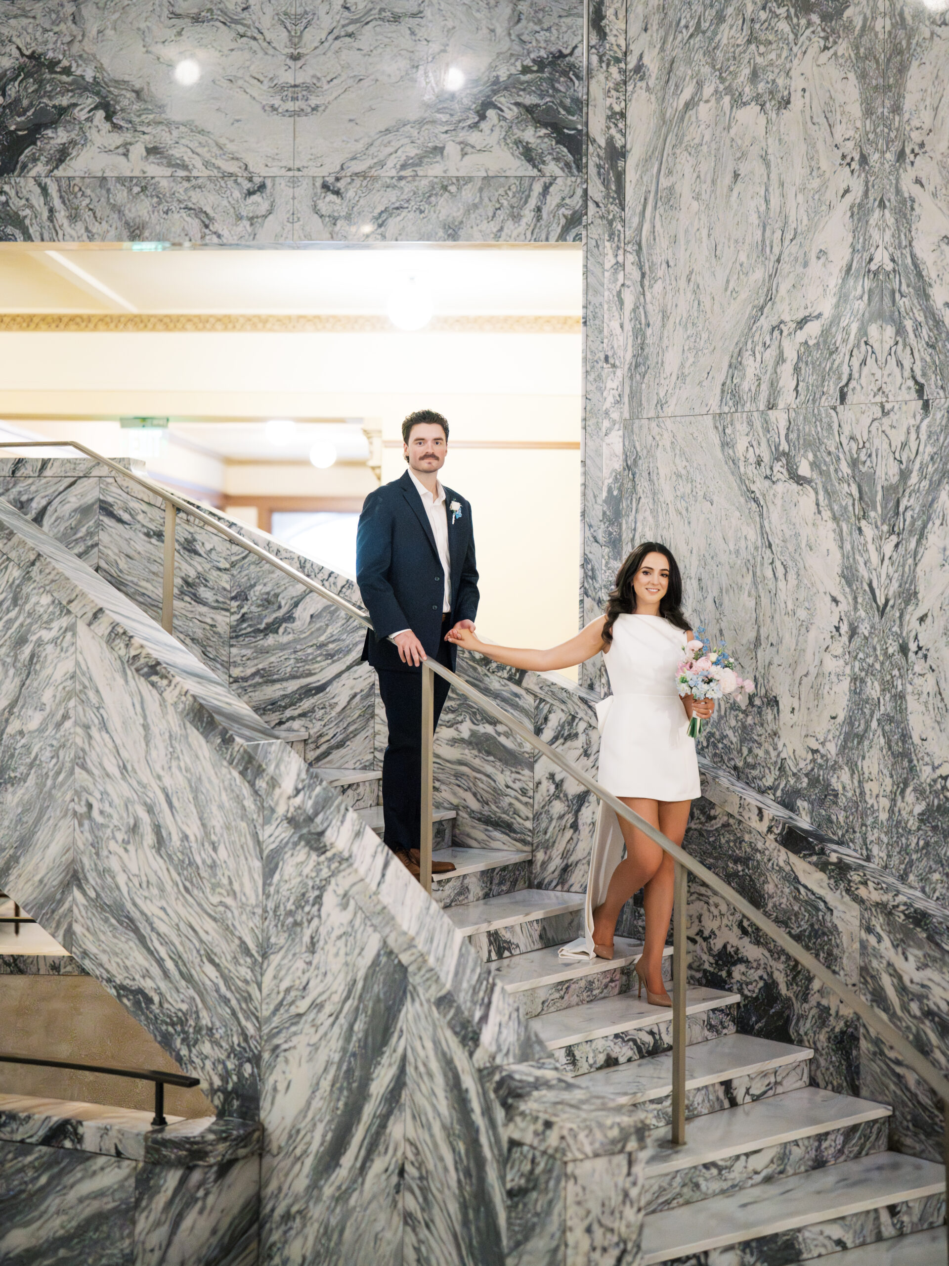 The bride and groom walking down the marble stairs together after their courthouse wedding in houston.