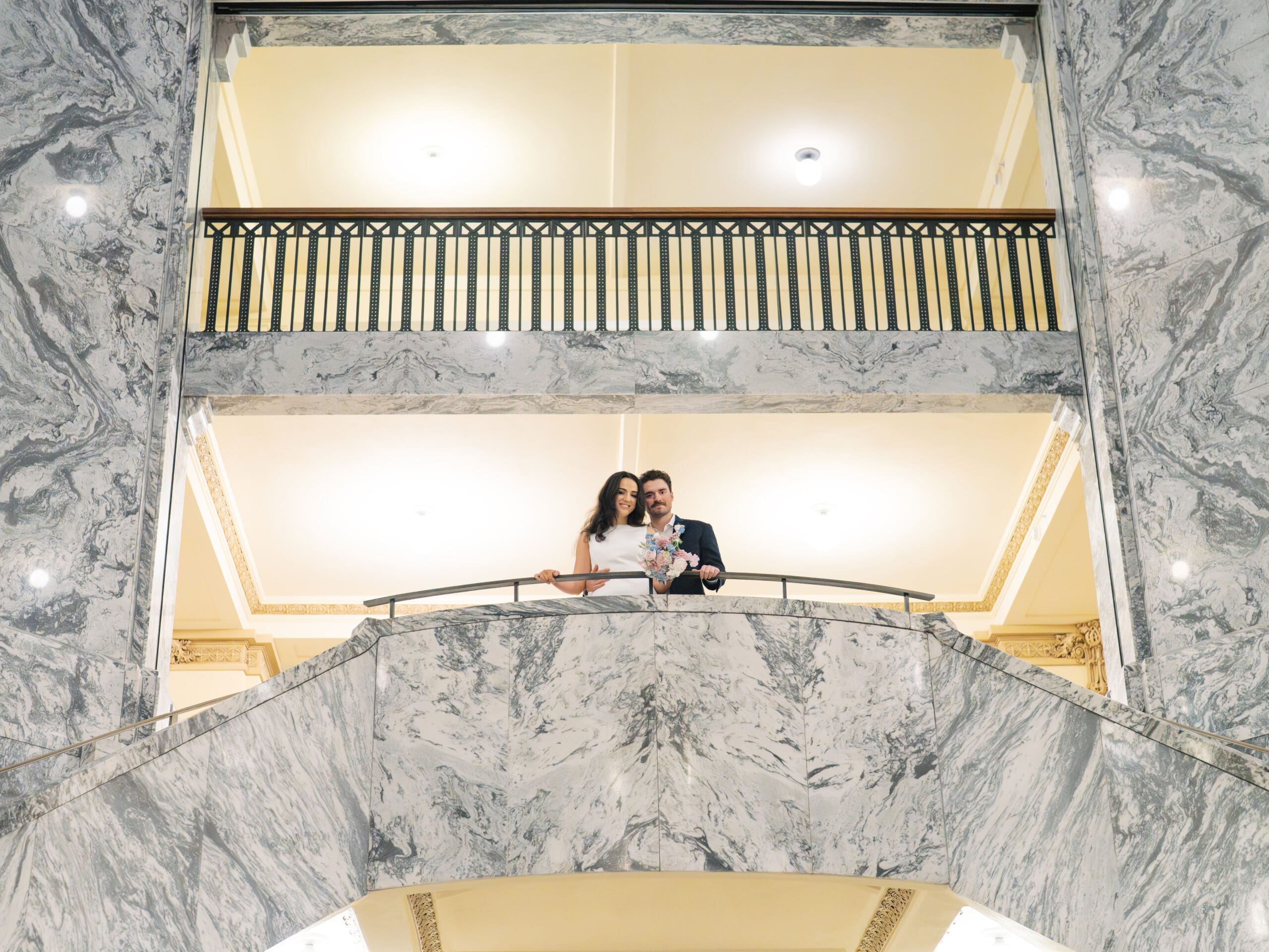 The bride and groom smiling and standing against a railing at the Houston courthouse smiling down at the photographer.