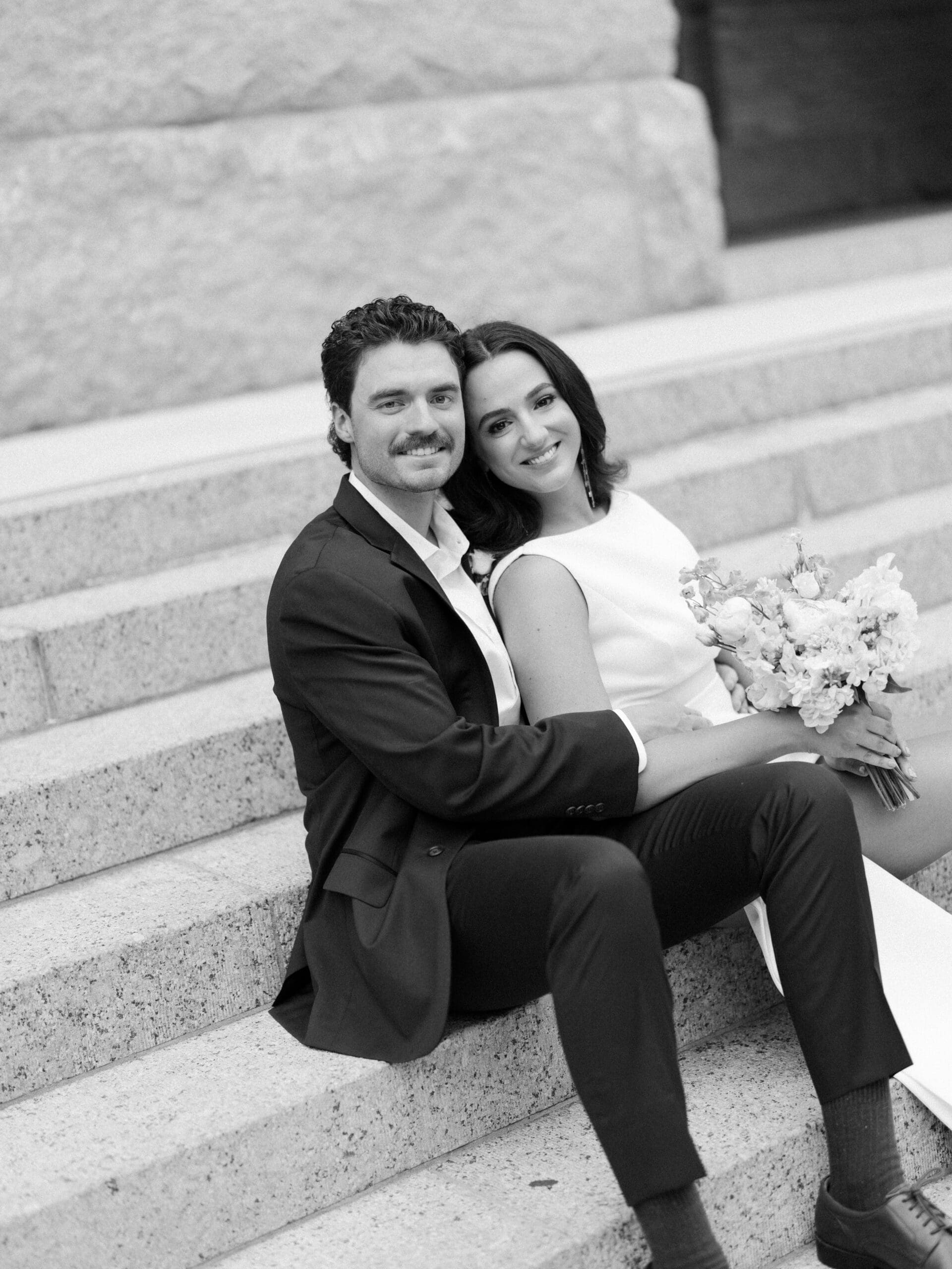 Bride and groom sitting together on granite steps smiling at the camera
