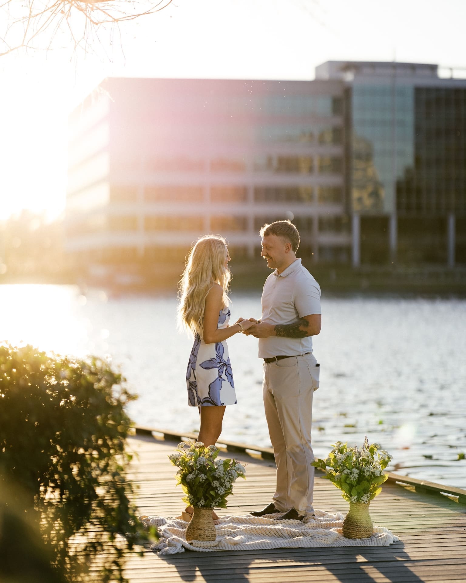 Newly engaged couple holding hands and smiling at each other surrounded by white florals on a Houston waterfront dock at golden hour