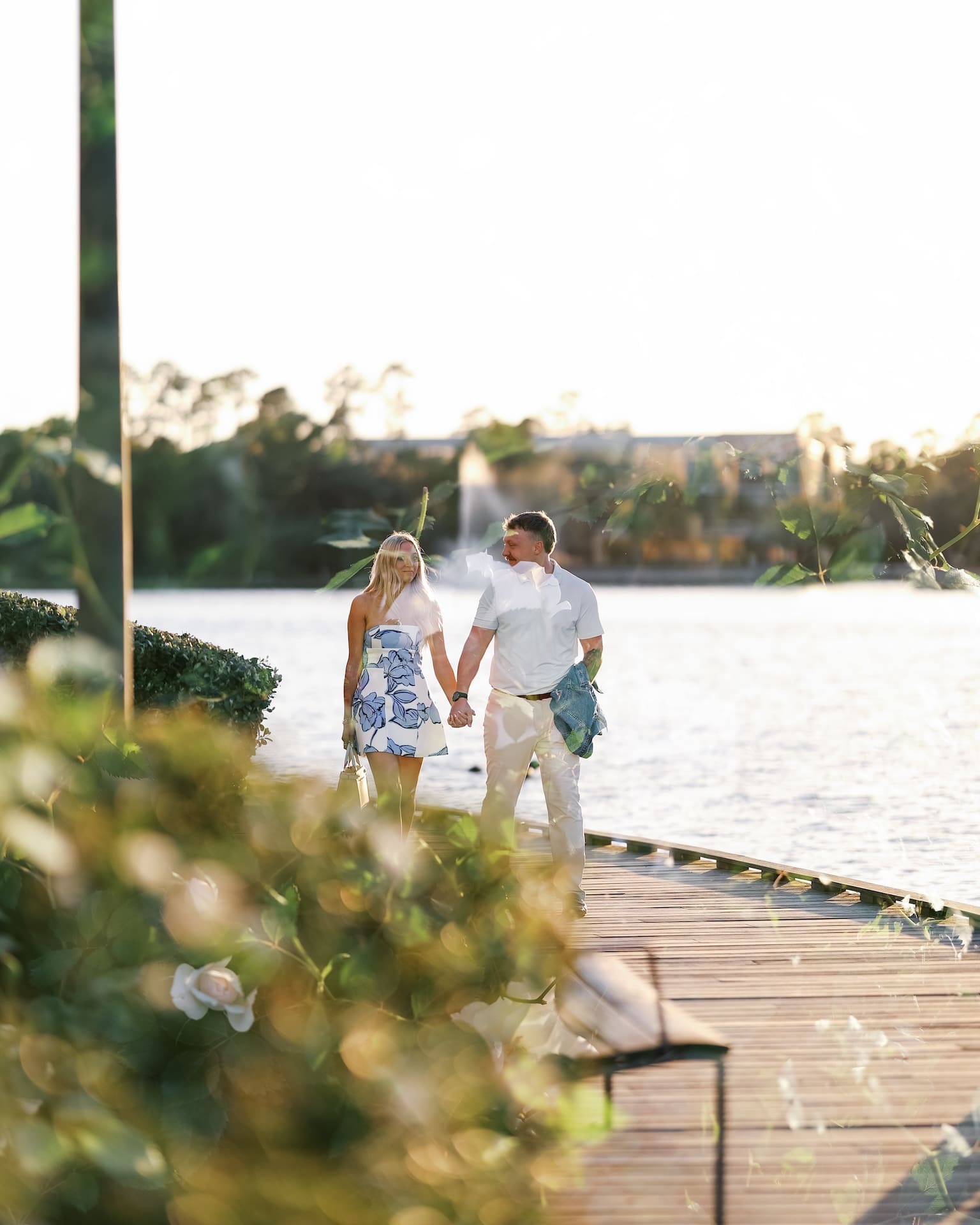 Couple walking hand in hand along a waterfront boardwalk at golden hour in Houston
