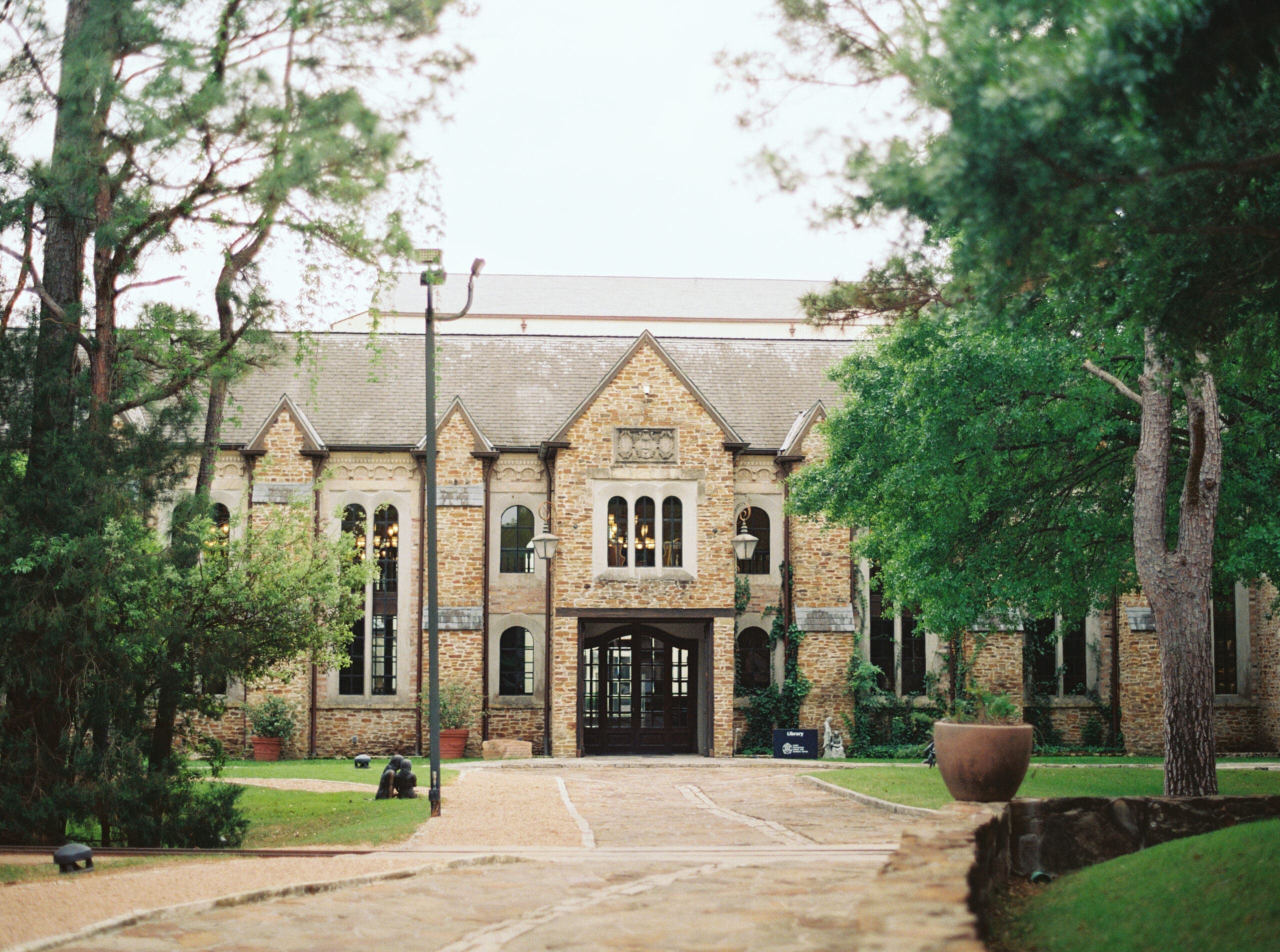 Exterior of The Lanier Theological Library surrounded by tall pine and oak trees, with warm light glowing through arched windows.
