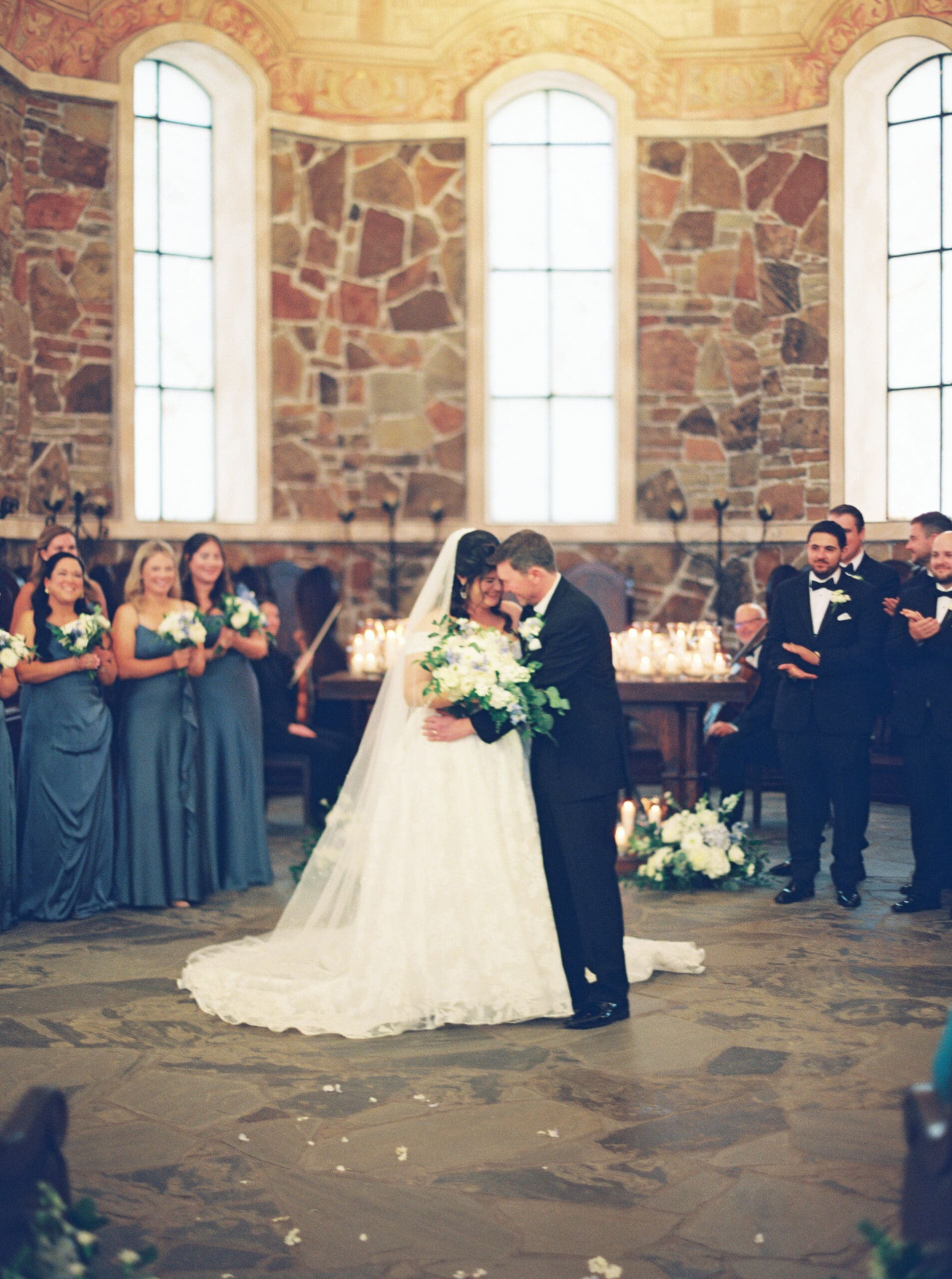 Bride and groom sharing a joyful moment at the altar of The Lanier Theological Library chapel, with candlelight and stone walls behind them as guests applaud.