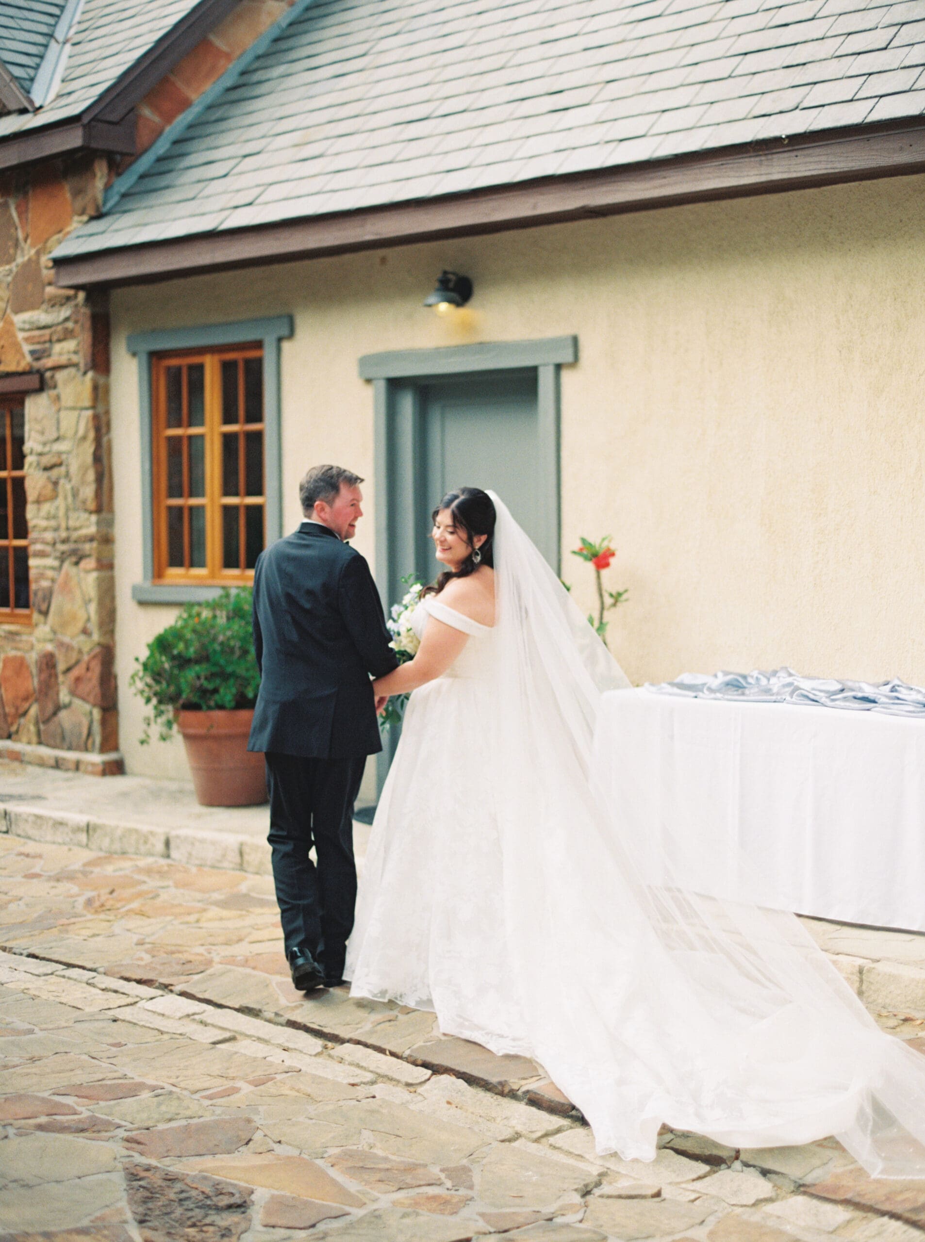 Bride and groom holding hands and sharing a sweet moment on the cobblestone patio outside The Lanier Theological Library.
