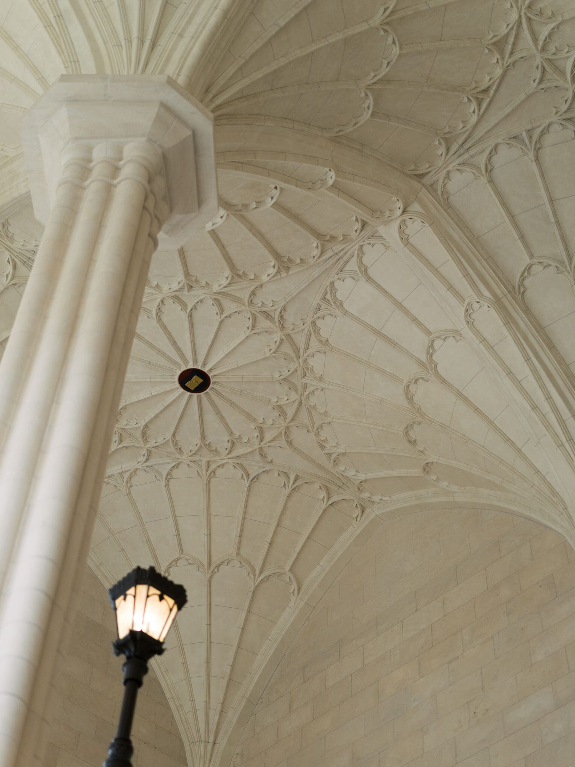 Looking up at the intricate fan-vaulted Gothic ceiling of The Lanier Theological Library, with a glowing gas lantern in the corner of the frame.