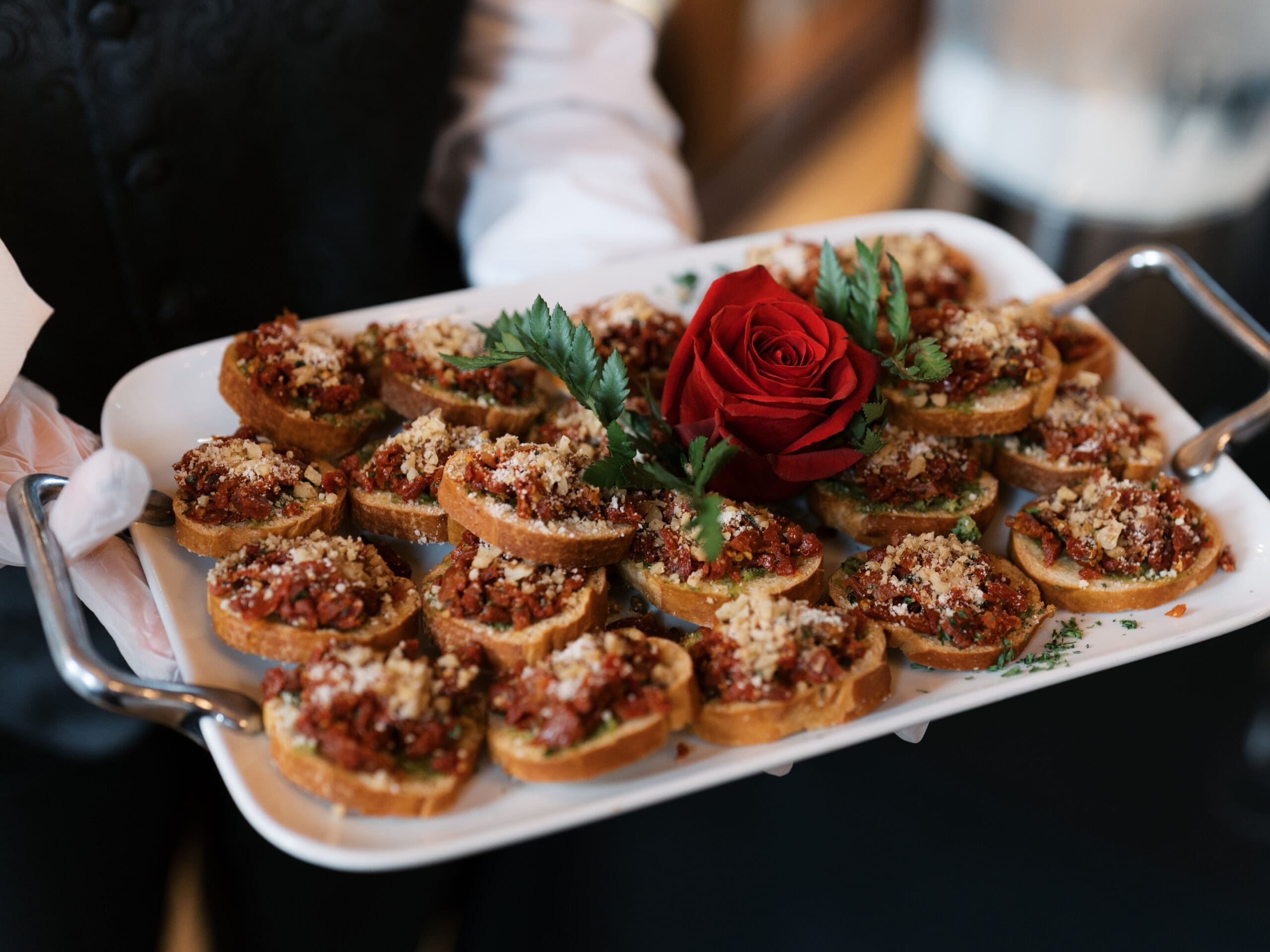 A white-gloved server presenting a tray of bruschetta appetizers garnished with a red rose at The Lanier Theological Library wedding reception.
