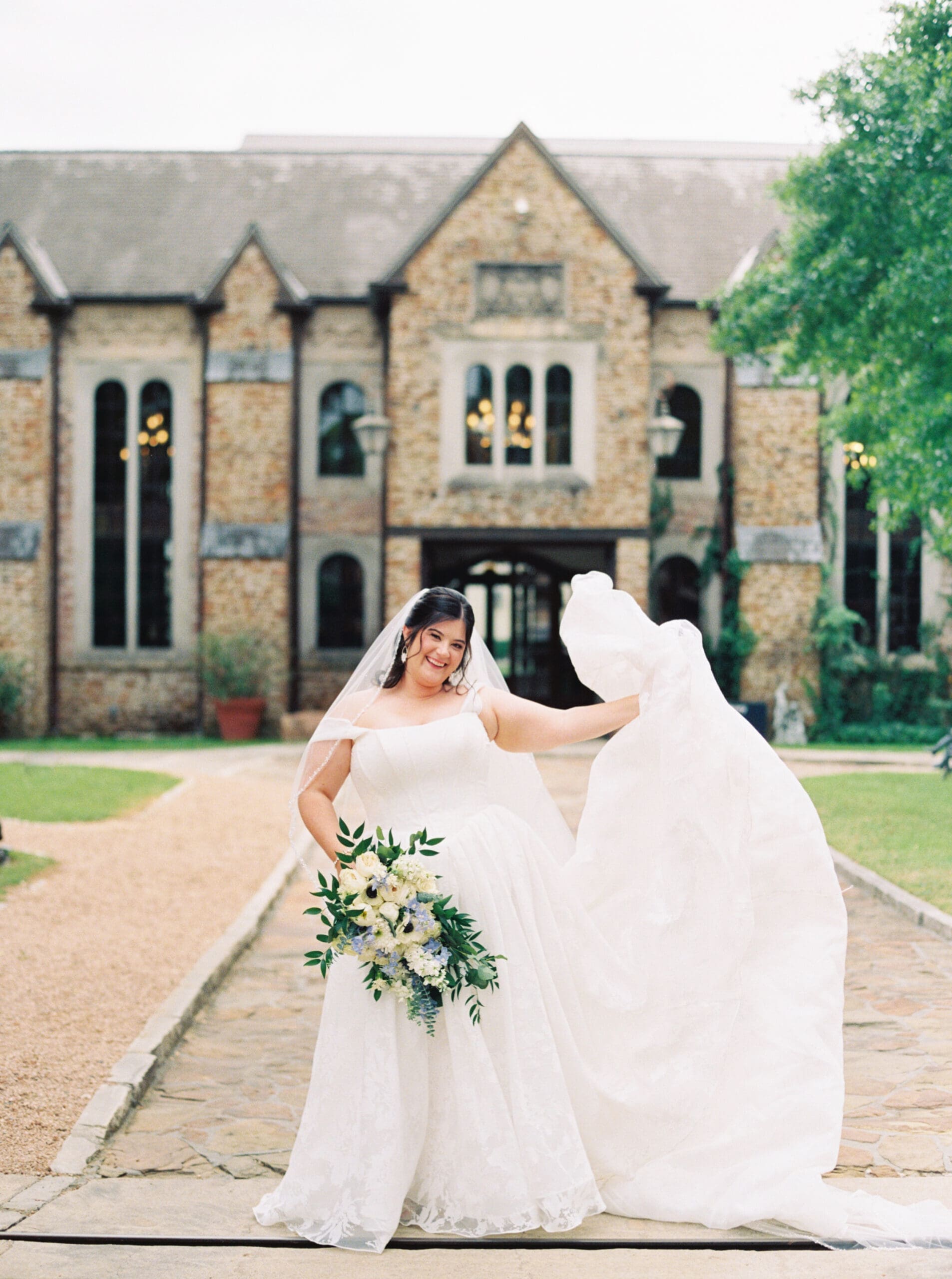 Bride joyfully tossing her dress in the air in front of The Lanier Theological Library entrance, her bouquet in hand and a huge smile on her face.