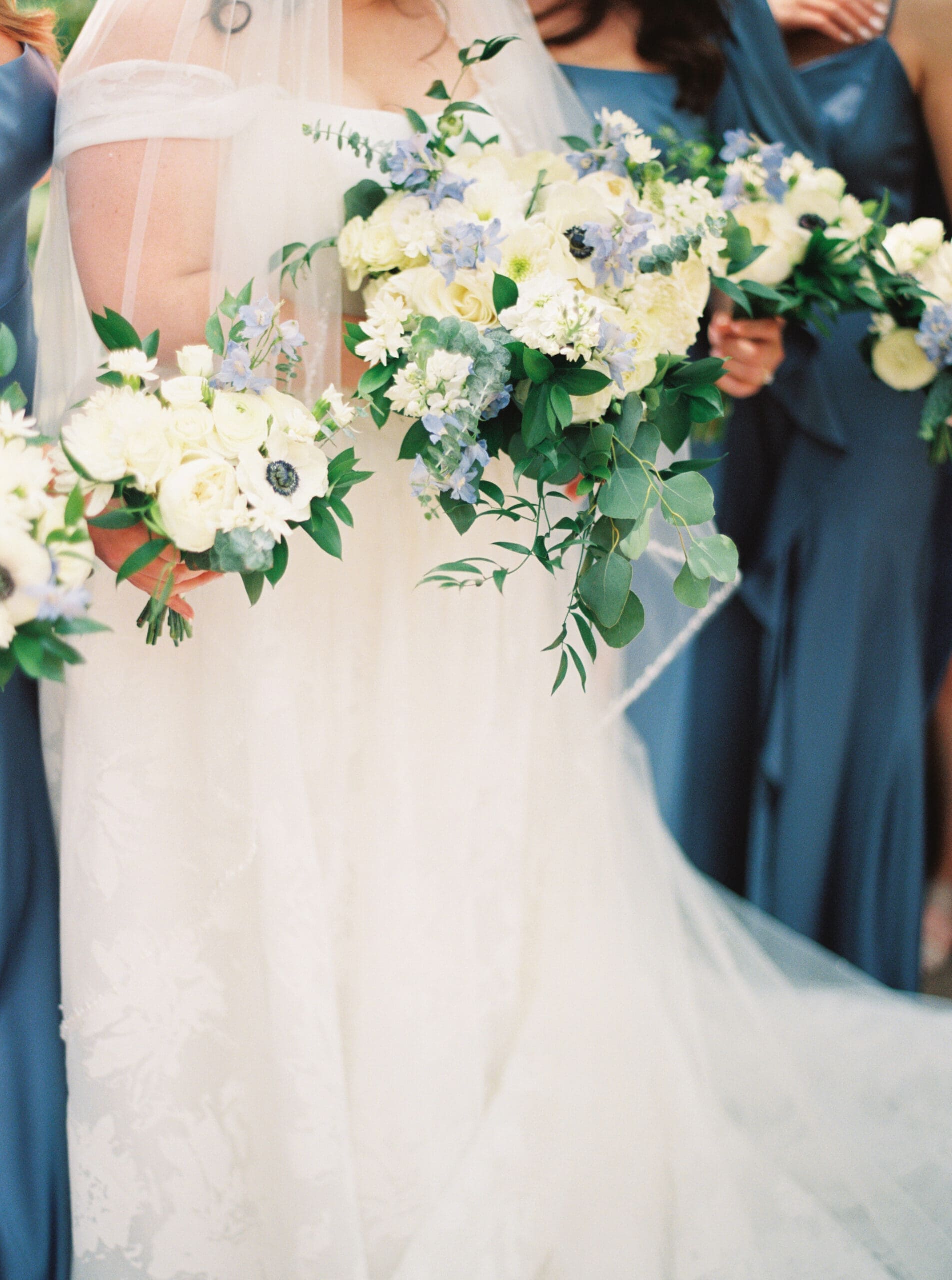 Close-up of the bridal party holding lush white and blue bouquets featuring roses, anemones, and cascading greenery.
