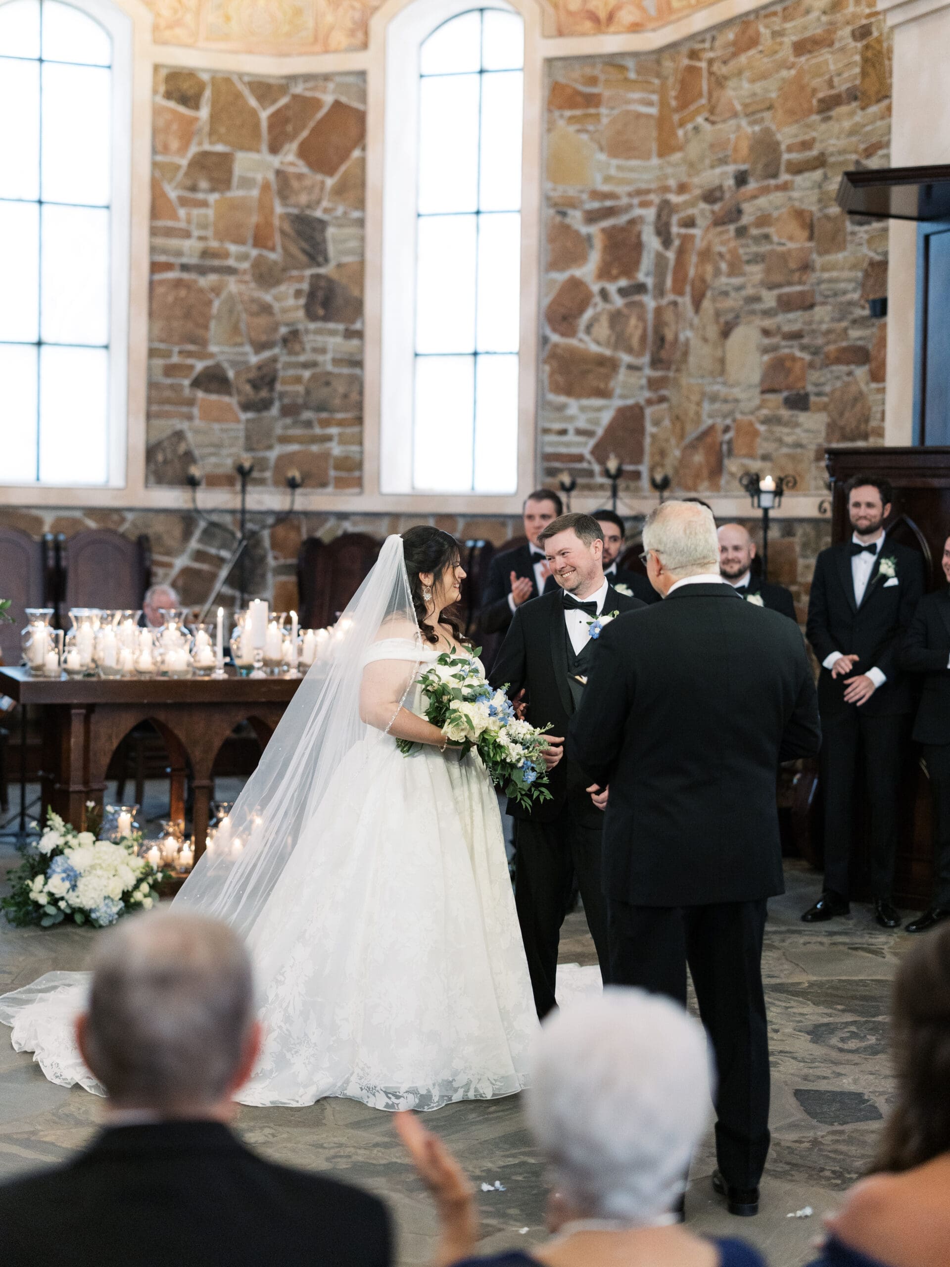 Bride and groom sharing a joyful moment at the altar of The Lanier Theological Library chapel, with candlelight and stone walls behind them as guests applaud.