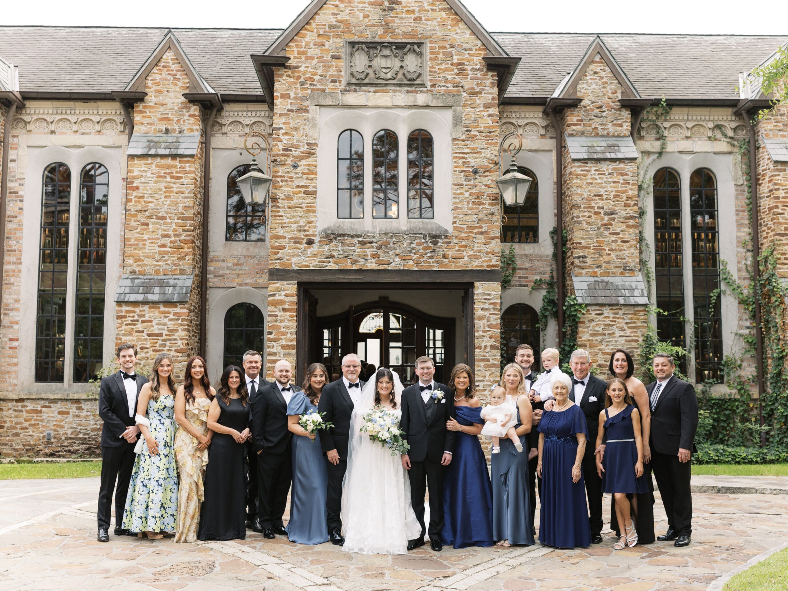 Wedding party and family gathered for a formal group portrait in front of the ivy-covered stone facade of The Lanier Theological Library.
