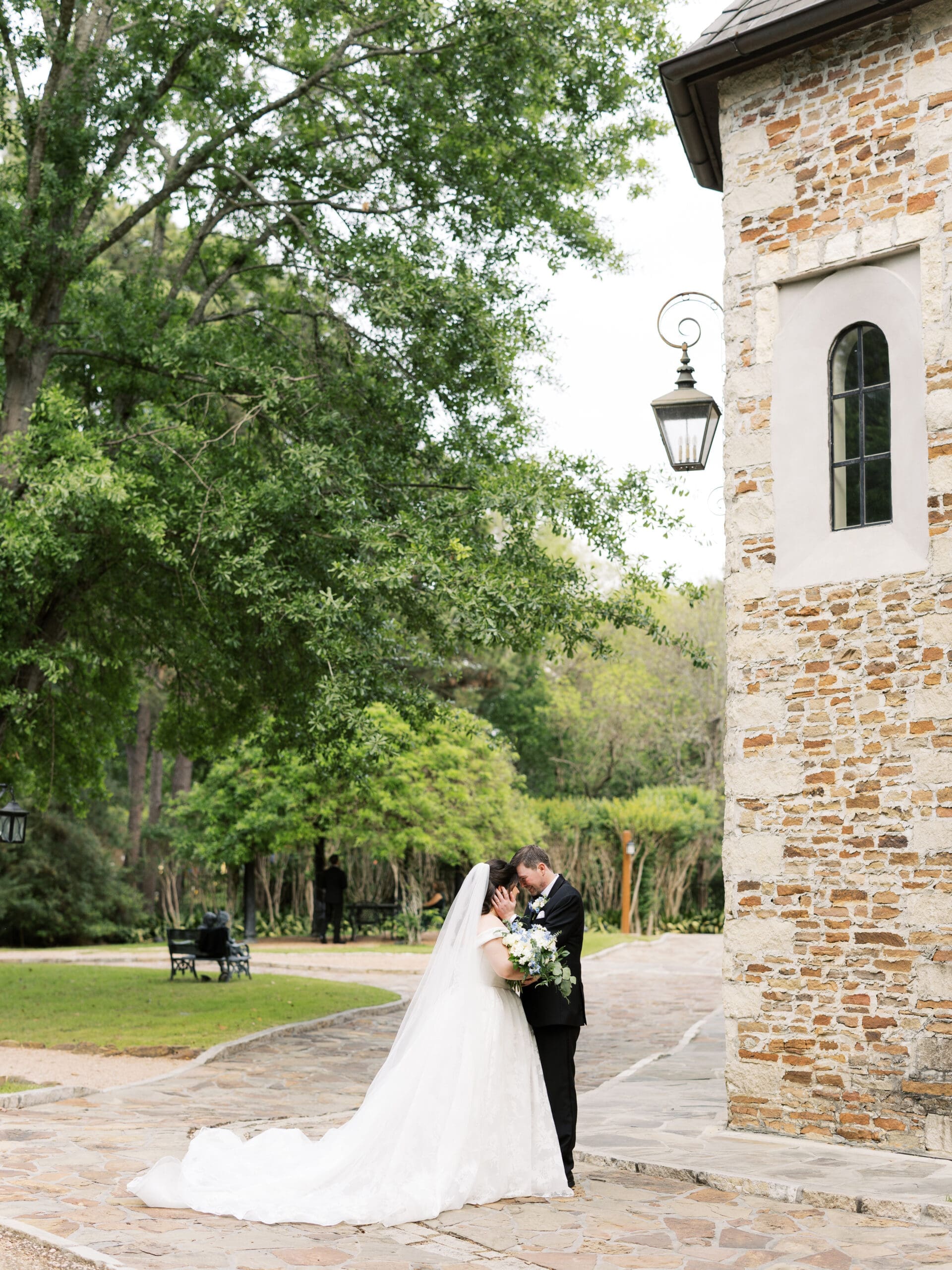 Bride and groom sharing an intimate forehead-to-forehead moment on the stone courtyard of The Lanier Theological Library, surrounded by lush green trees.
