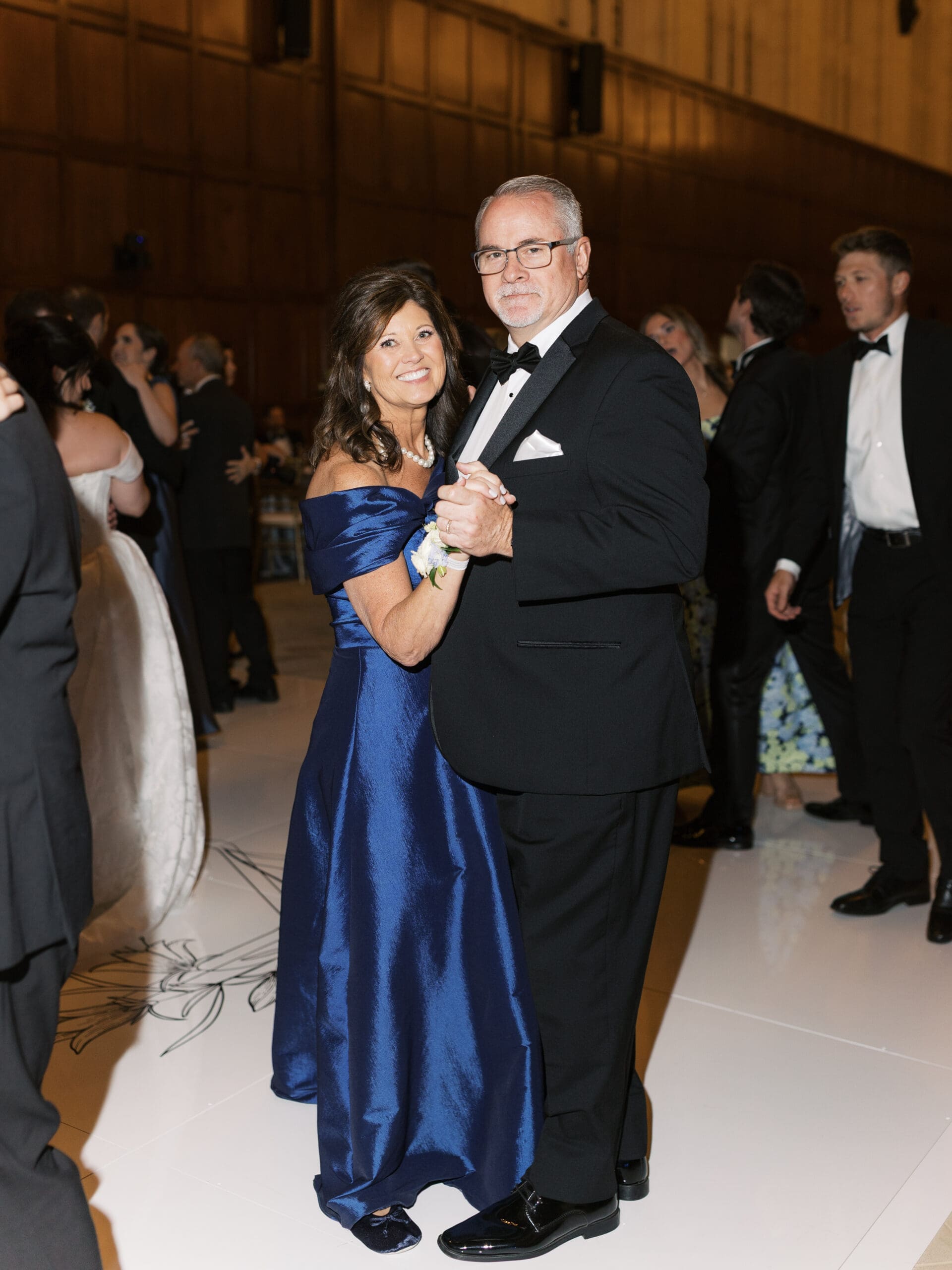 Mother of the bride in a navy off-shoulder gown dancing with her husband at The Lanier Theological Library wedding reception, surrounded by other guests on the dance floor.

