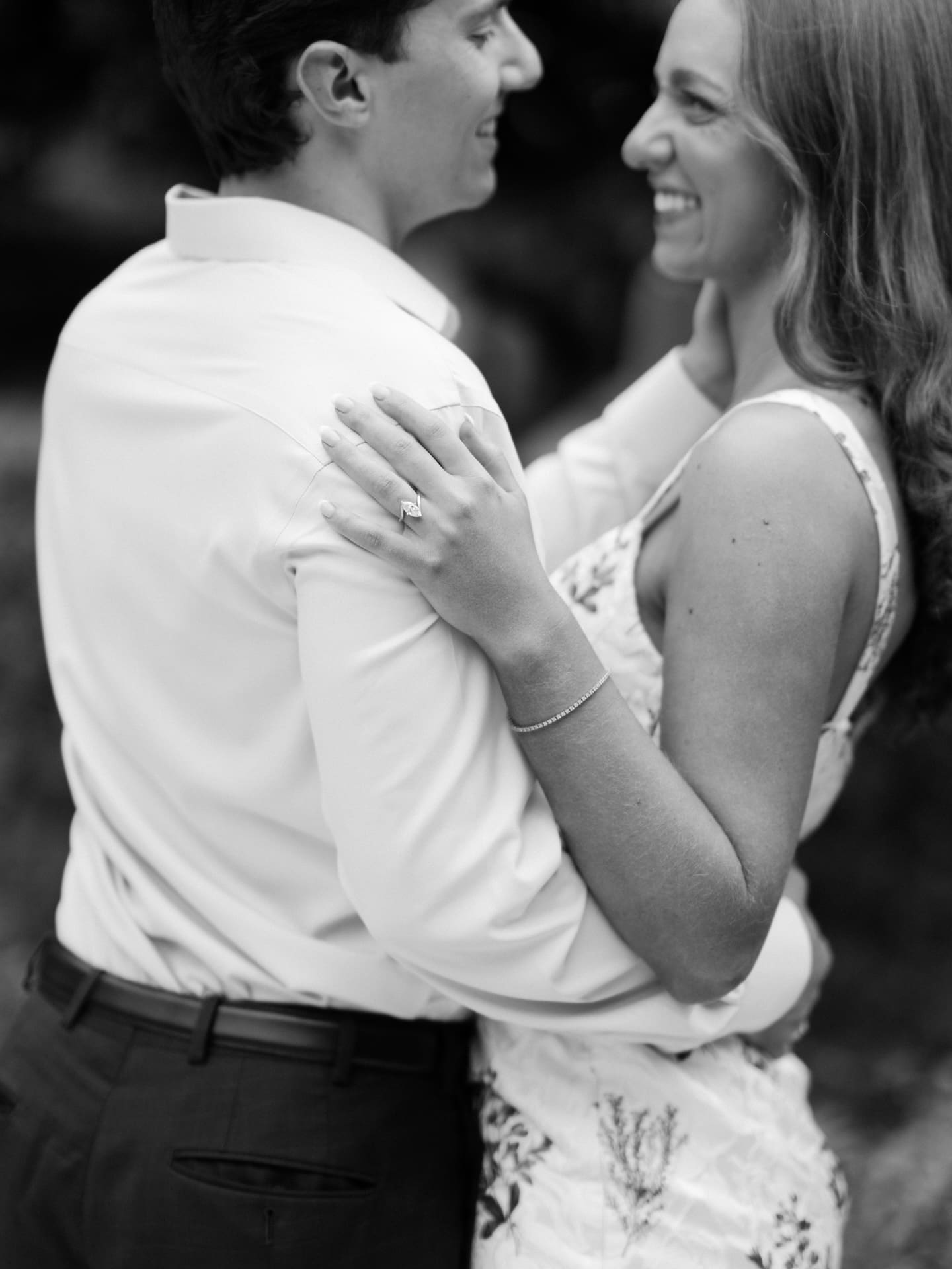 Close-up black and white shot of a bride-to-be's hand resting on her fiancé's shoulder, showing her engagement ring.